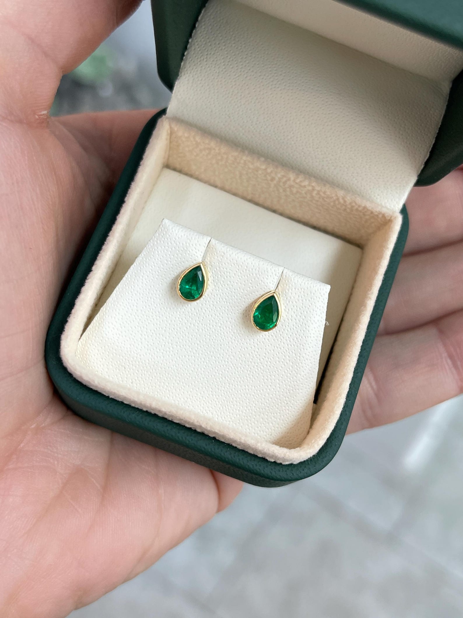 Rich green pear cut Zambian emerald stud earrings with 18K bezel setting by JR Colombian Emeralds, shown in close-up image.