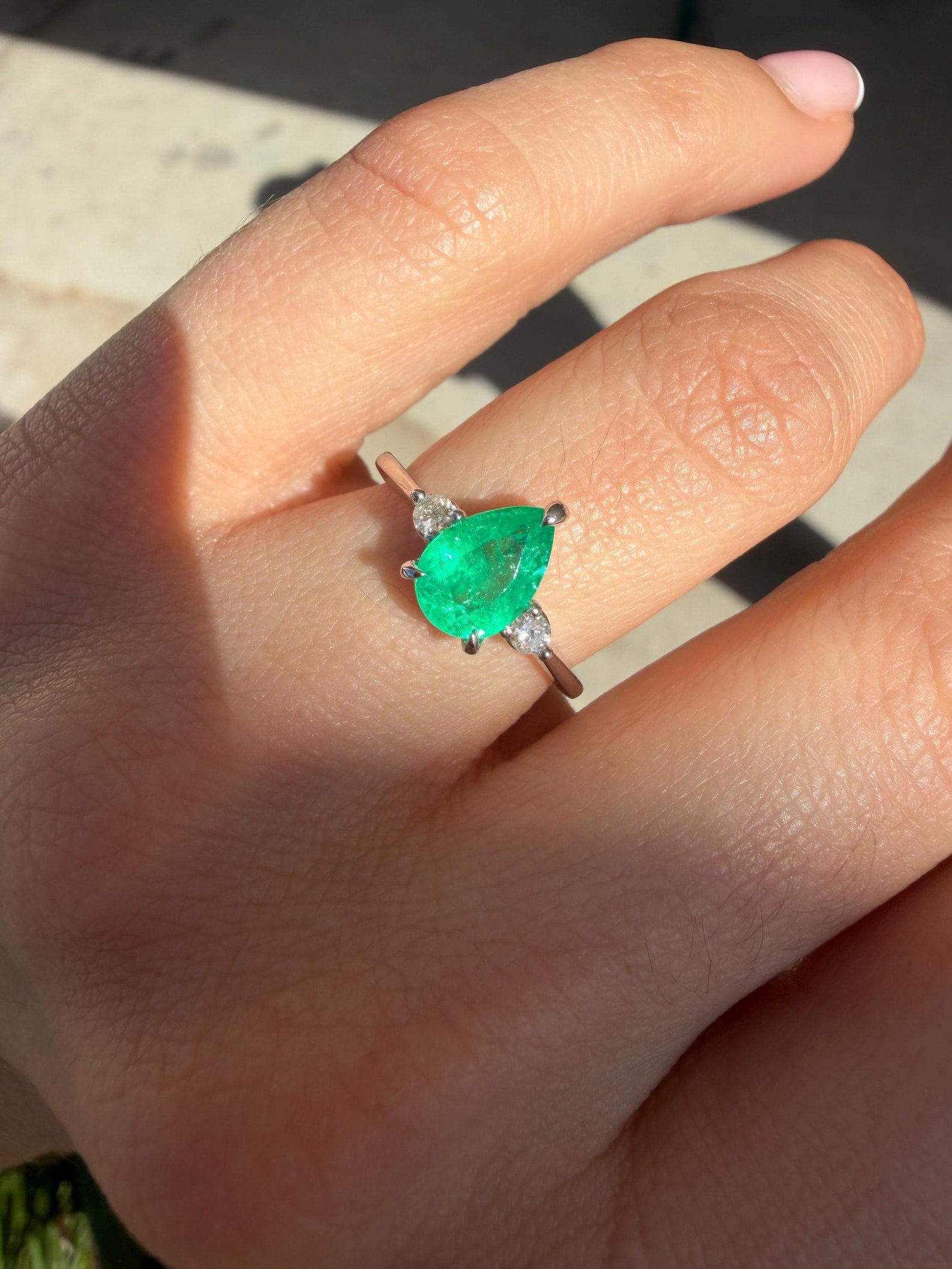 Pear cut Colombian emerald three stone engagement ring with platinum prong setting, featuring vibrant green emeralds and elegant design.
