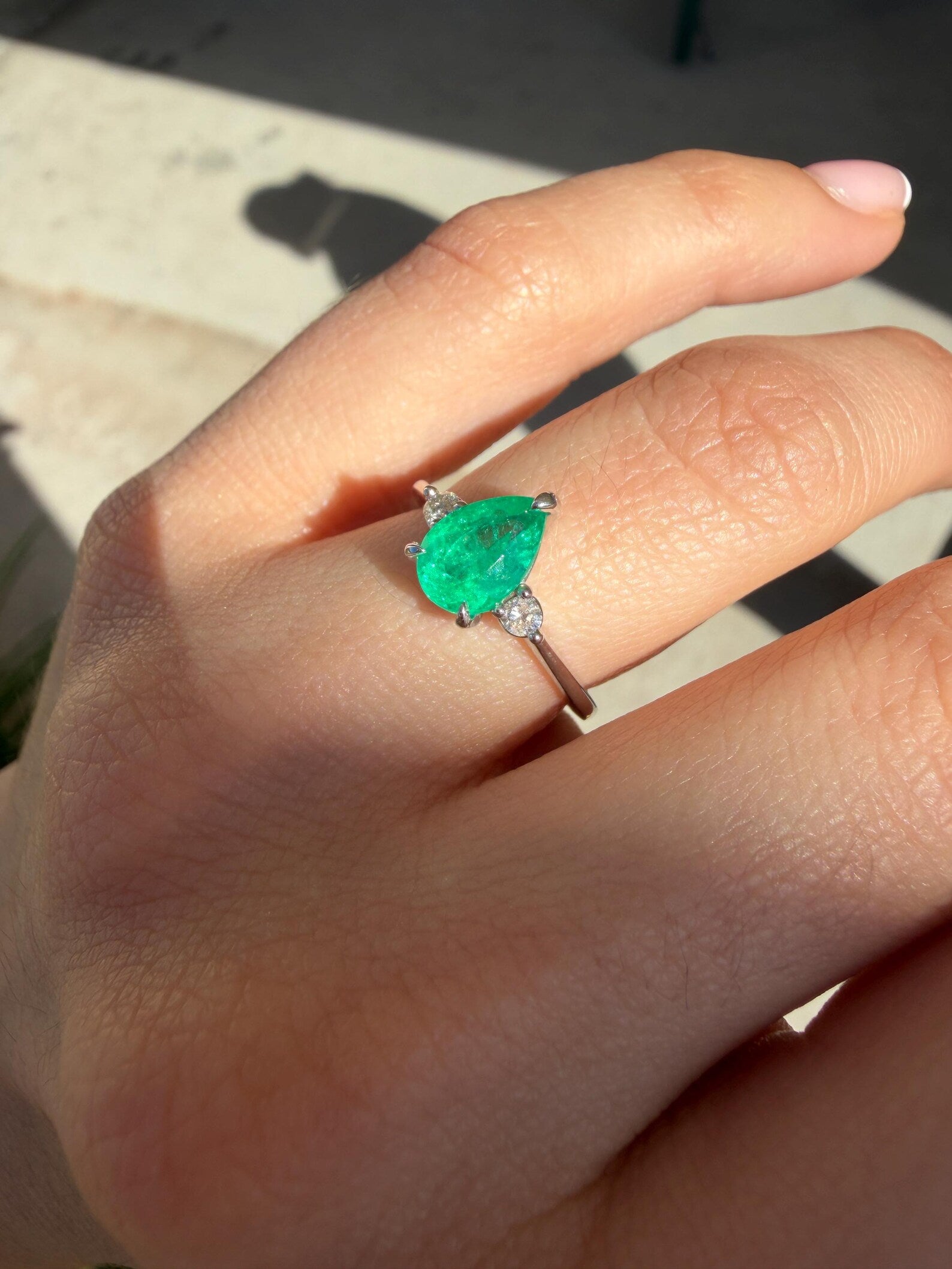 Pear-shaped Colombian emerald three-stone engagement ring with platinum prong setting, showcasing vibrant green gemstones.