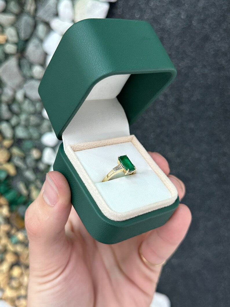 14K gold 2.45tcw dark green emerald and diamond accents engagement ring featuring three stones and tapered baguette diamonds.