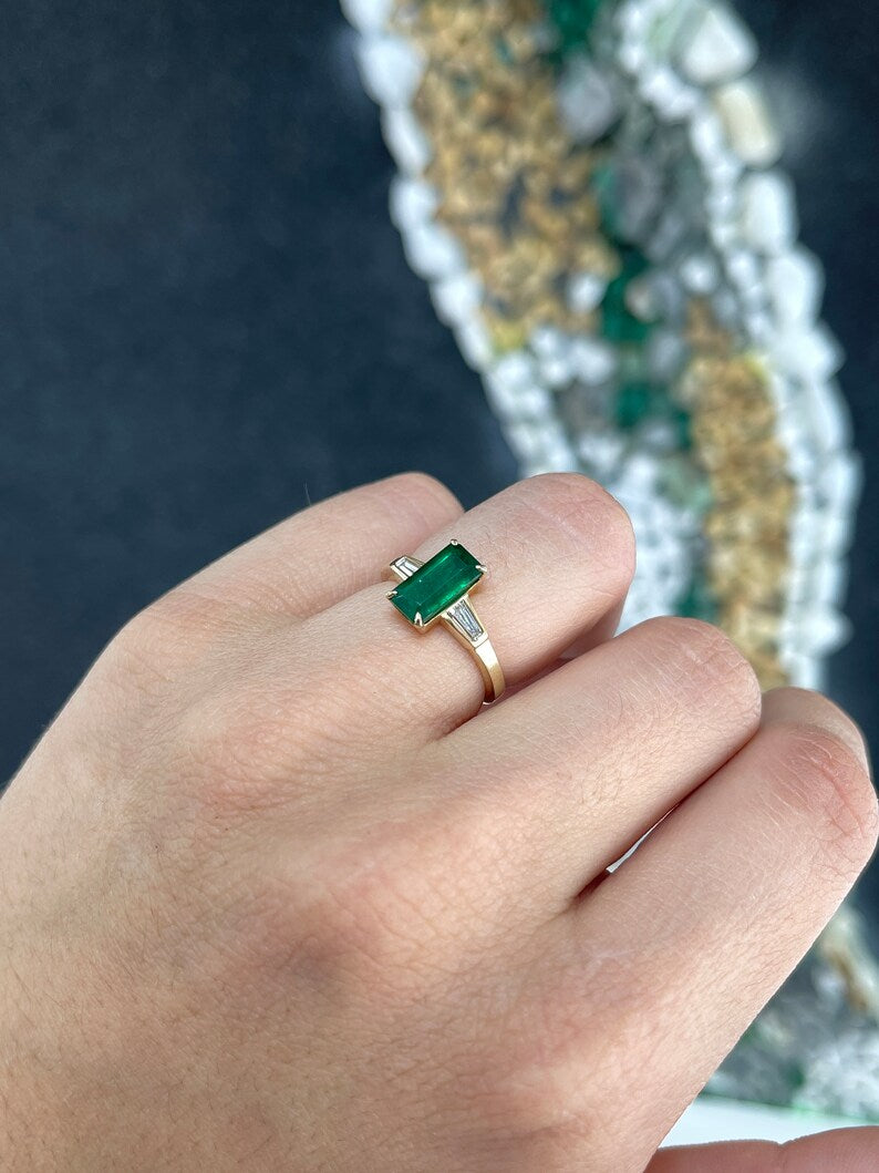14K gold engagement ring with dark green emerald and tapered baguette diamond accents, featuring a three-stone design.