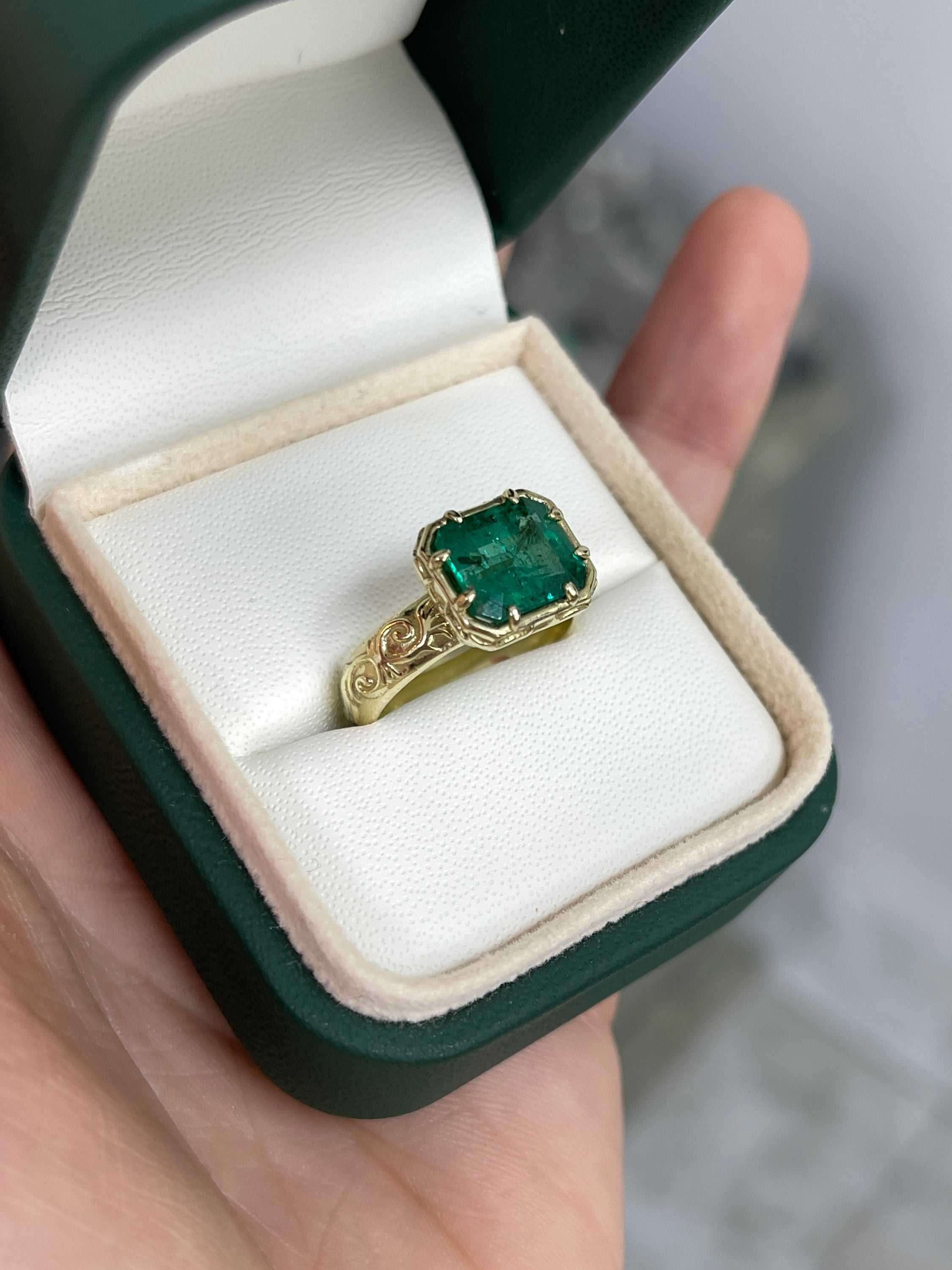 14K gold solitaire emerald ring featuring a 3.65ct east-to-west freckled earth-mined emerald with scroll and etched gold details.