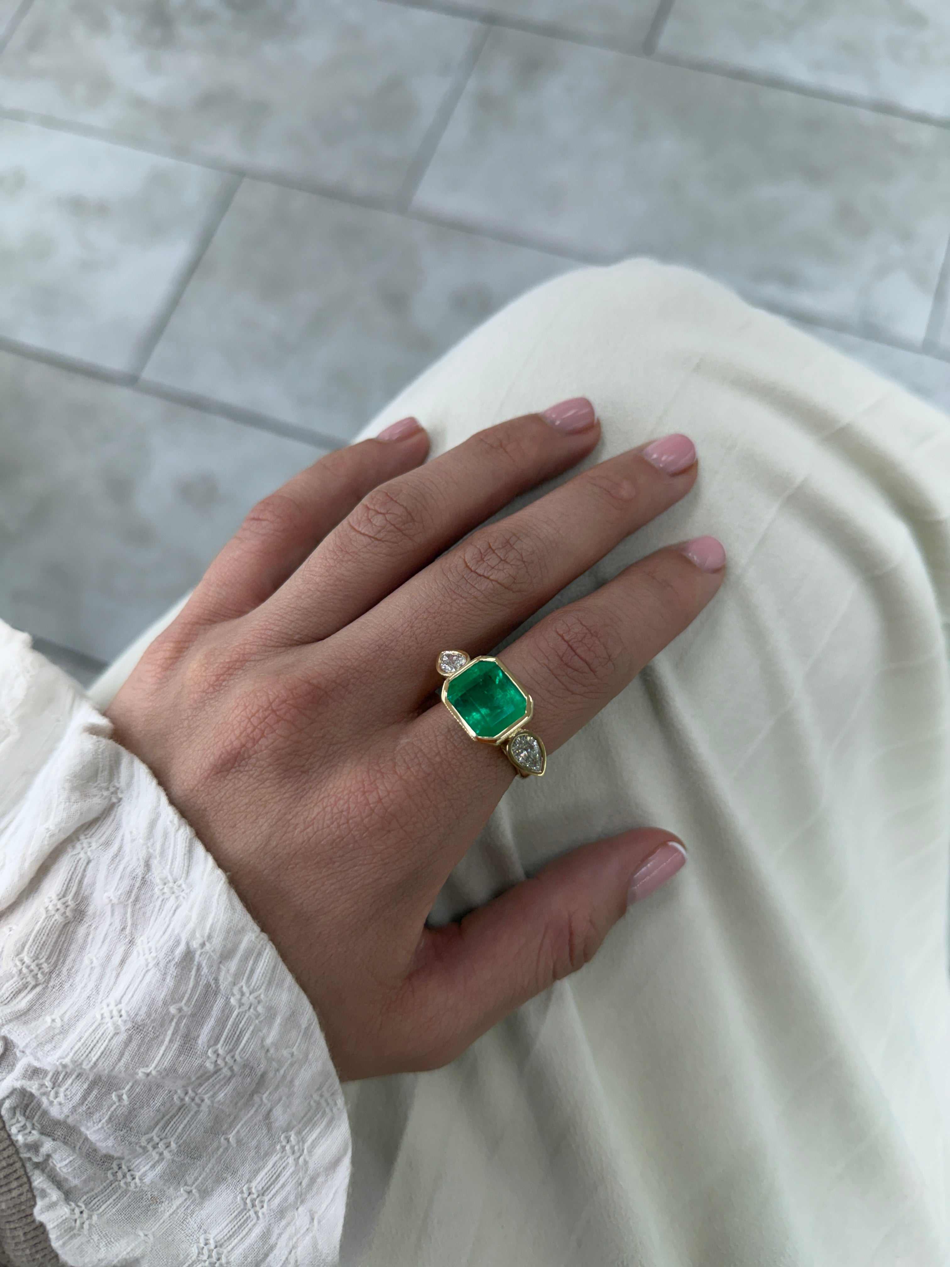 East to West Colombian emerald and pear diamond three-stone ring in 18K gold, featuring vibrant green emeralds and sparkling diamonds.