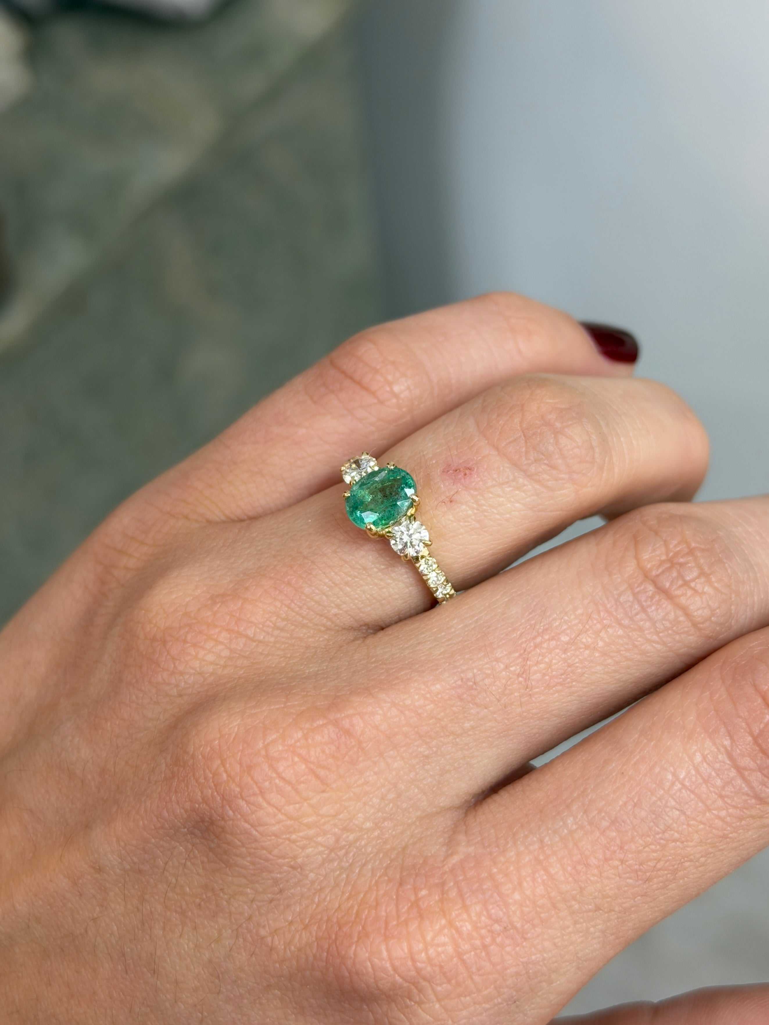 14K gold three-stone ring with 2.40tcw oval emerald and round lab diamonds, accented with additional small diamonds.