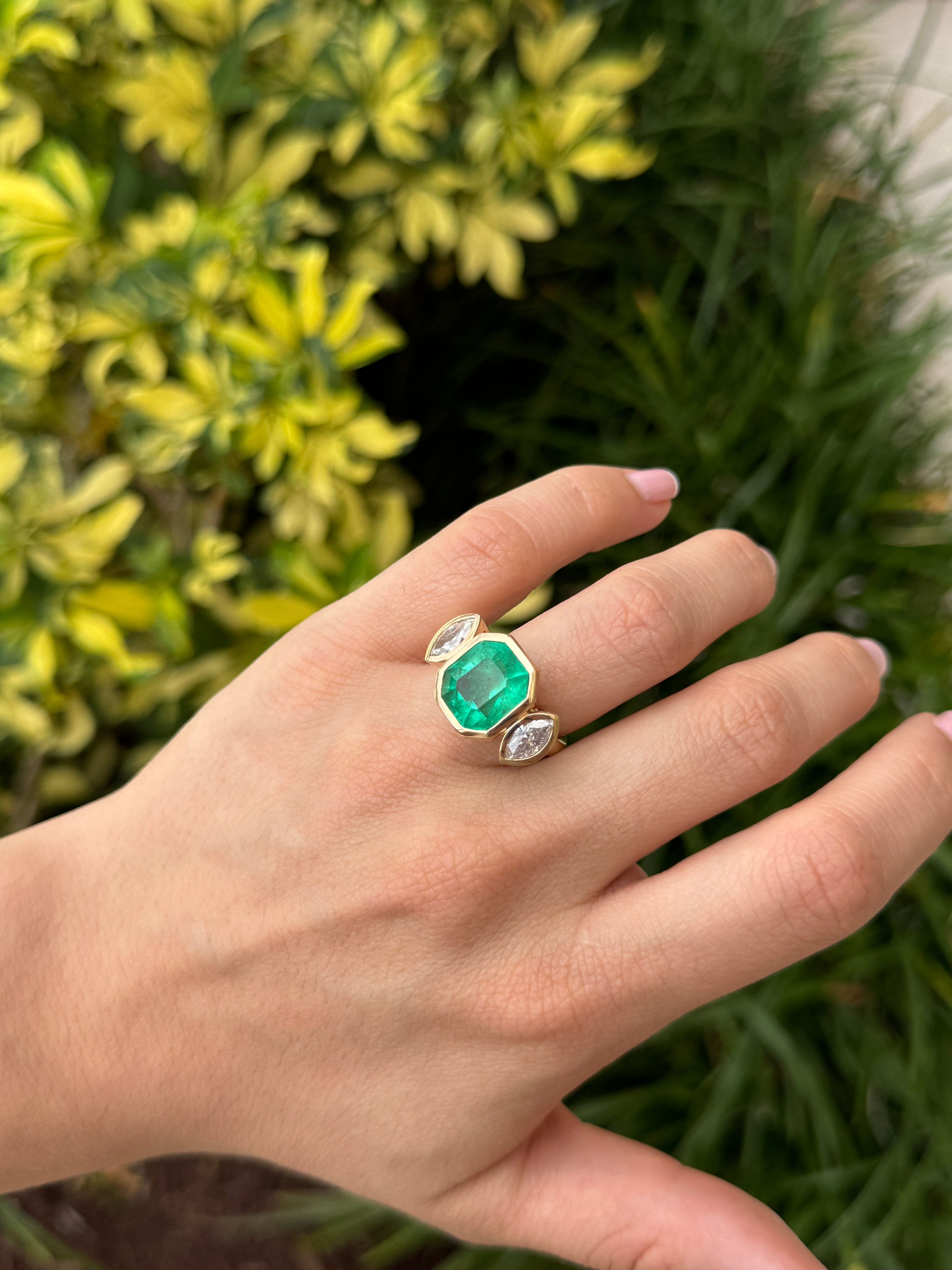 Emerald cut Colombian emerald and marquise diamond trilogy ring in 18K gold, featuring intricate bezel settings and fine craftsmanship.