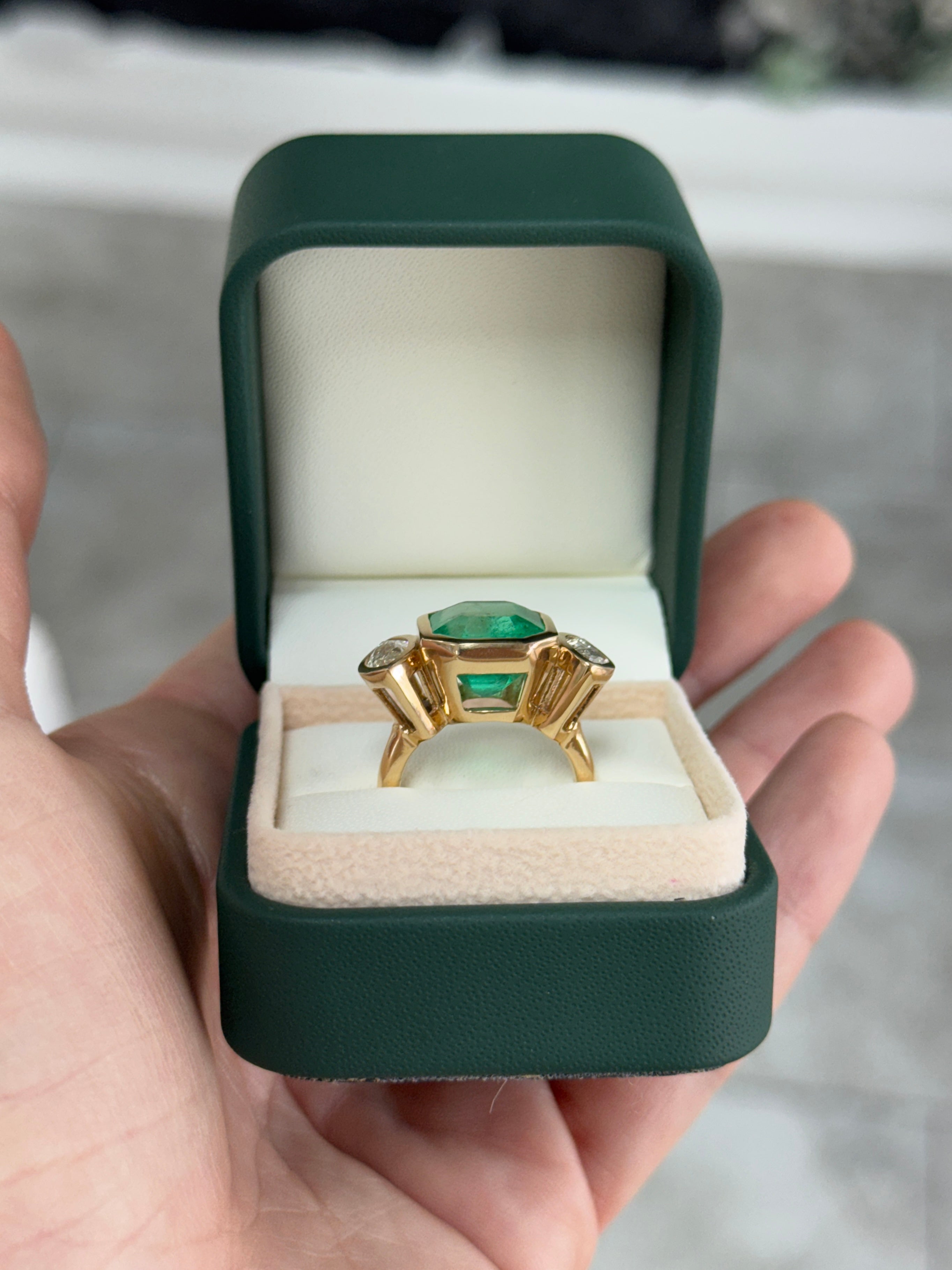 Emerald cut Colombian emerald and marquise diamond trilogy ring in 18K gold, featuring a 9.66tcw center emerald with bezel setting.