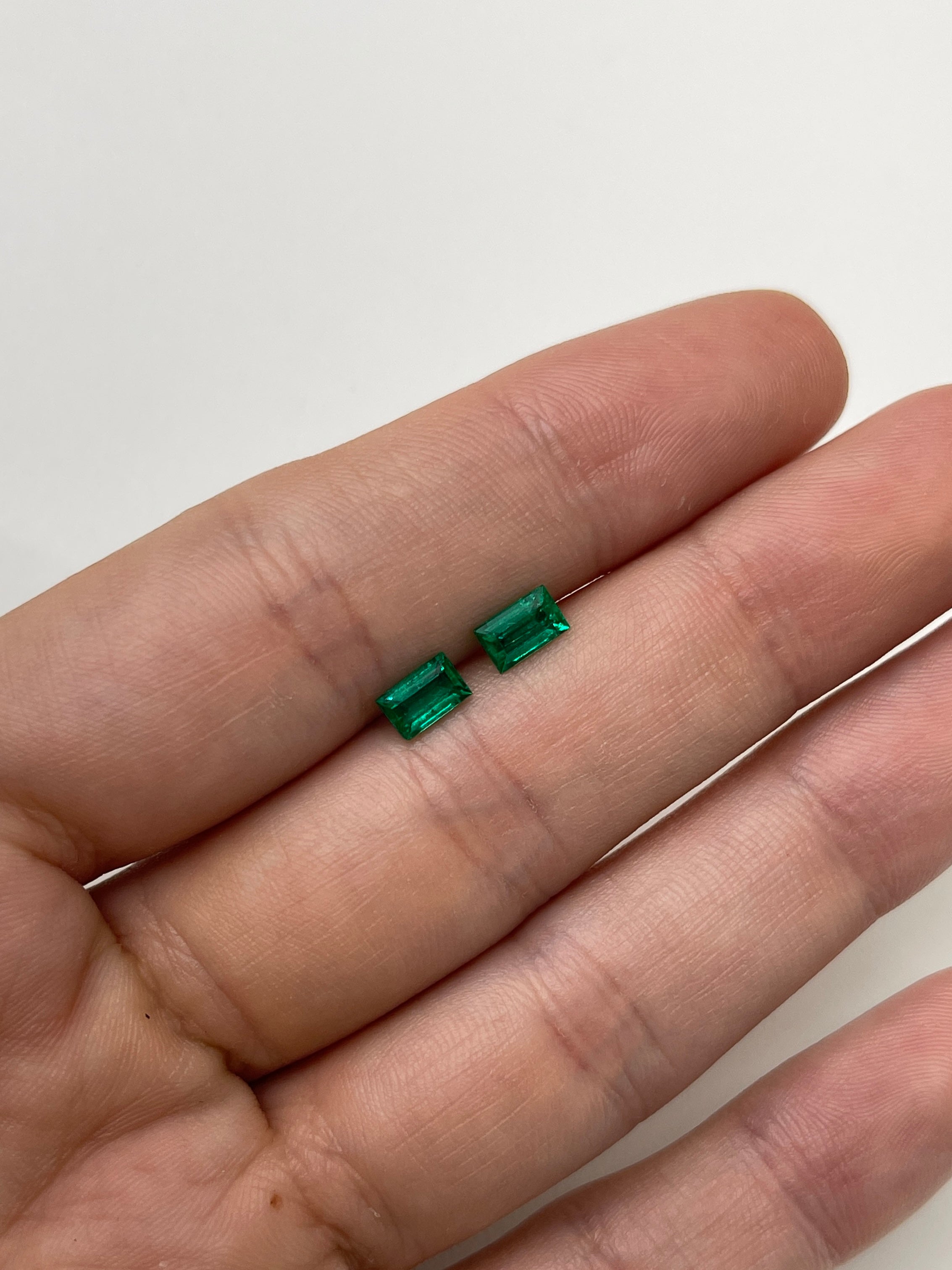Matching pair of 0.99tcw green Colombian emerald baguette cuts on a neutral background.