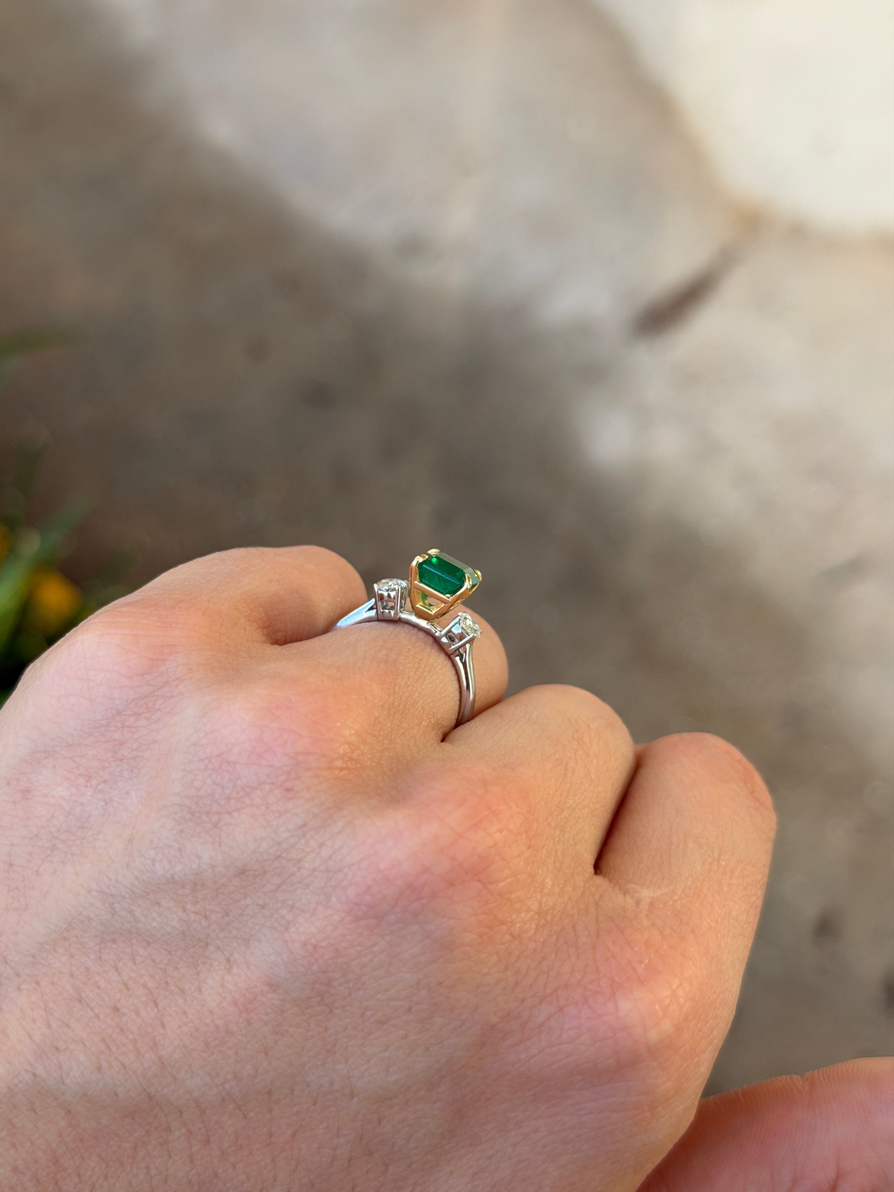 18K platinum ring featuring three-stone design with vivid emerald and diamond accents, showcasing Asscher and oval cuts.
