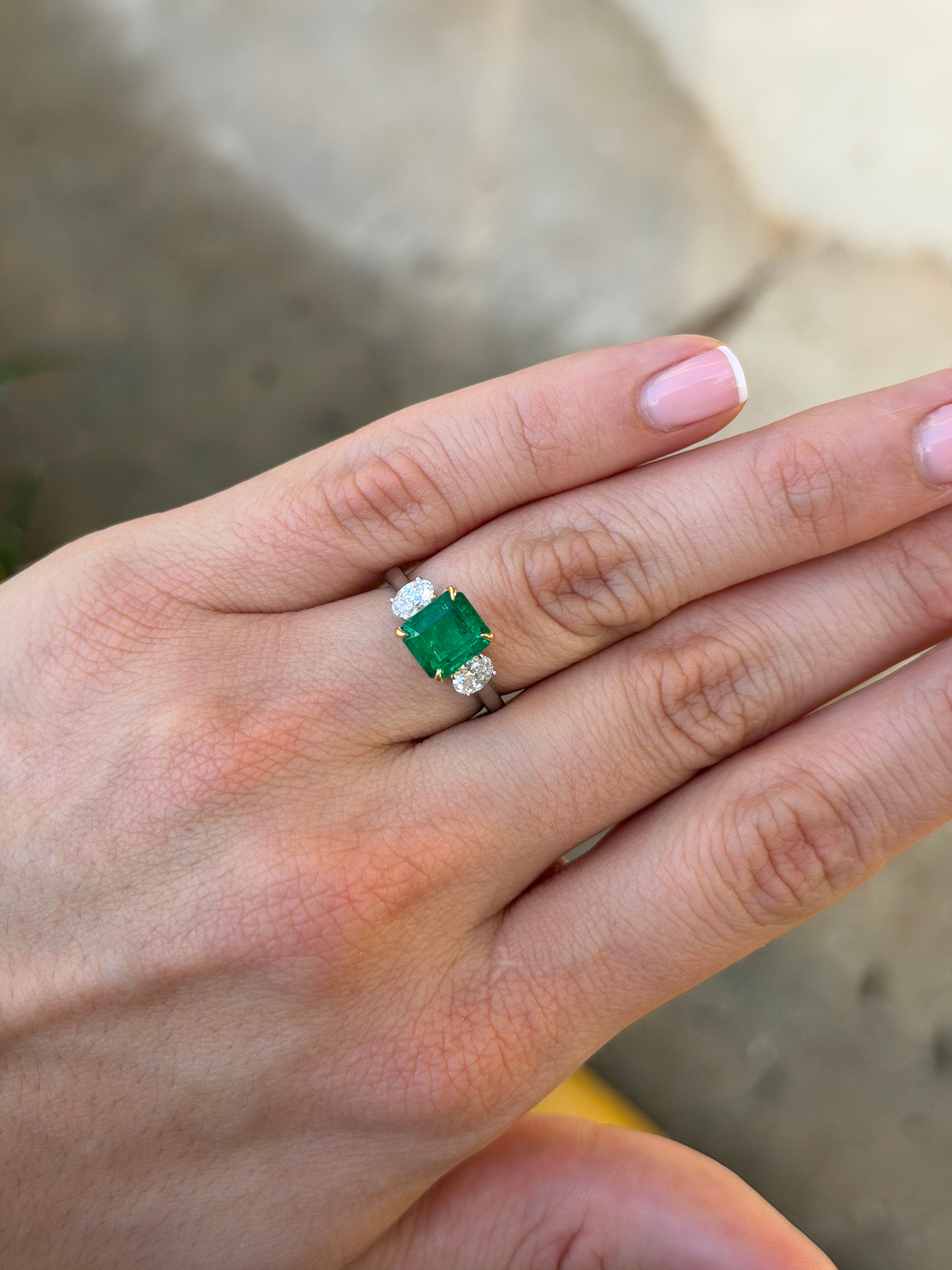 18K gold three-stone ring featuring vivid asscher-cut emeralds and oval diamonds, set in platinum, by JR Colombian Emeralds.