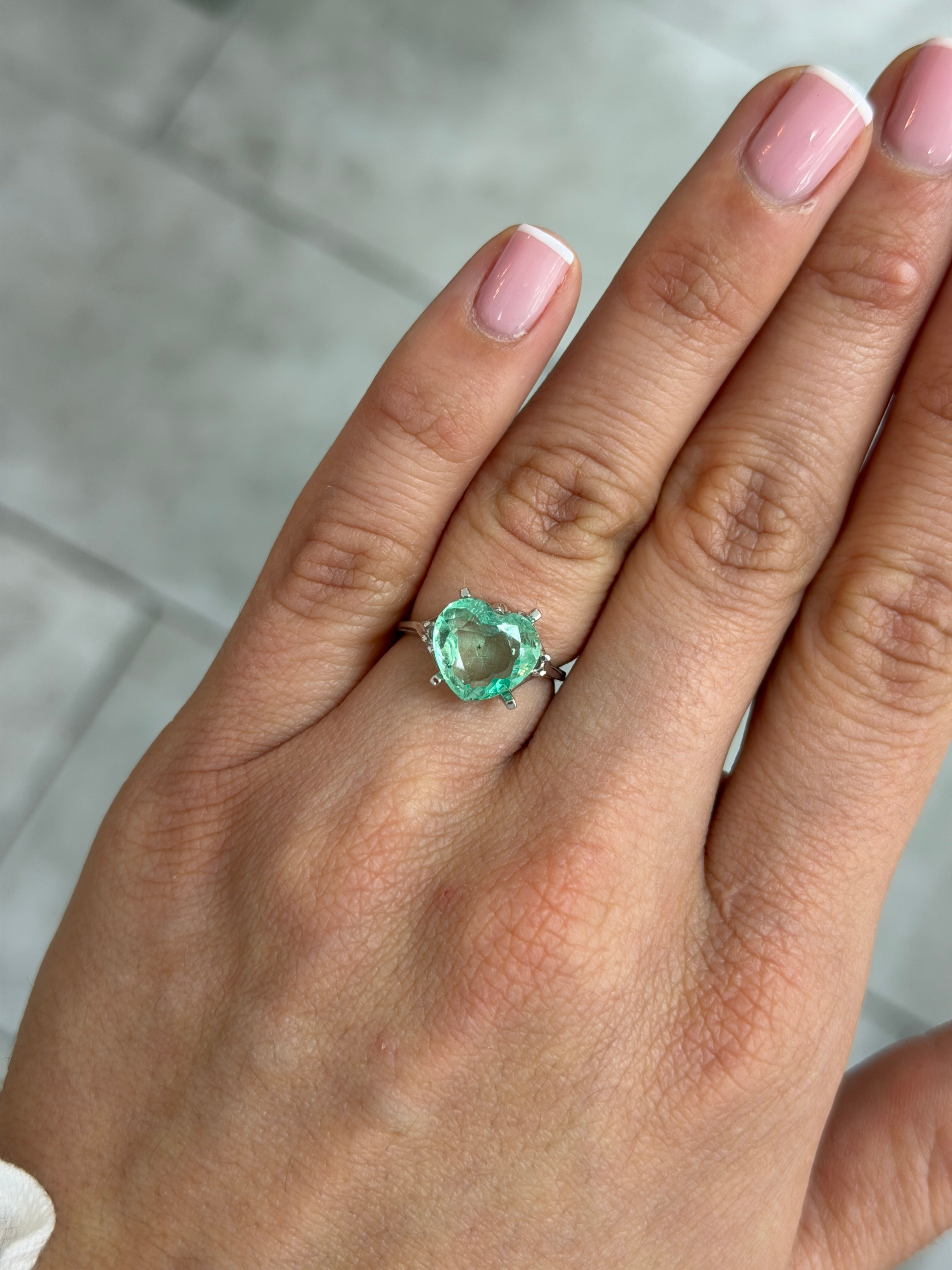 Light bluish-green Colombian emerald in 10x11 portrait cut with natural freckles, heart shape, loose gemstone from JR Colombian Emeralds.