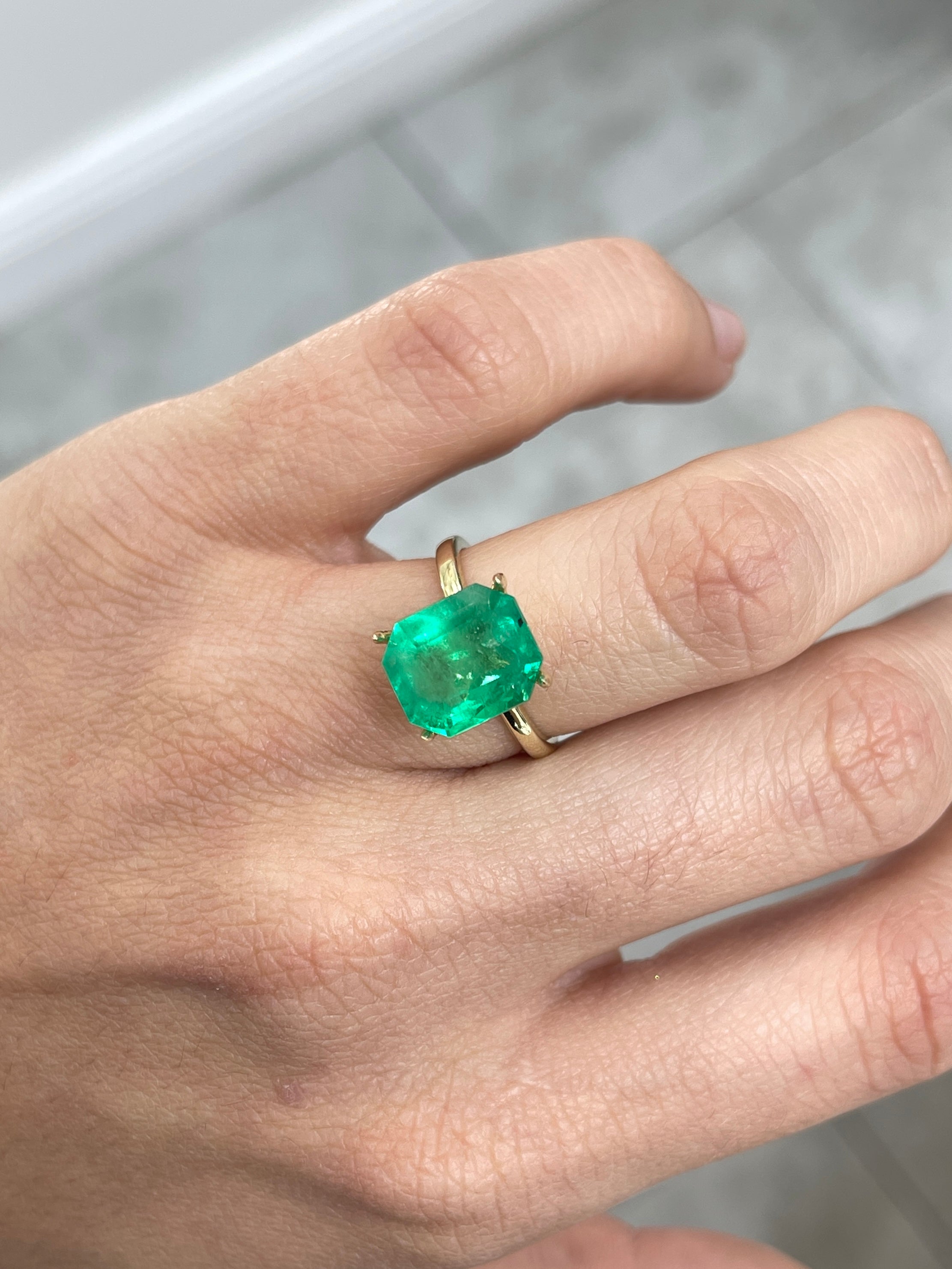 Freckled 5.75 carat medium green Colombian emerald loose gemstone in emerald cut, showcasing natural color and facets.