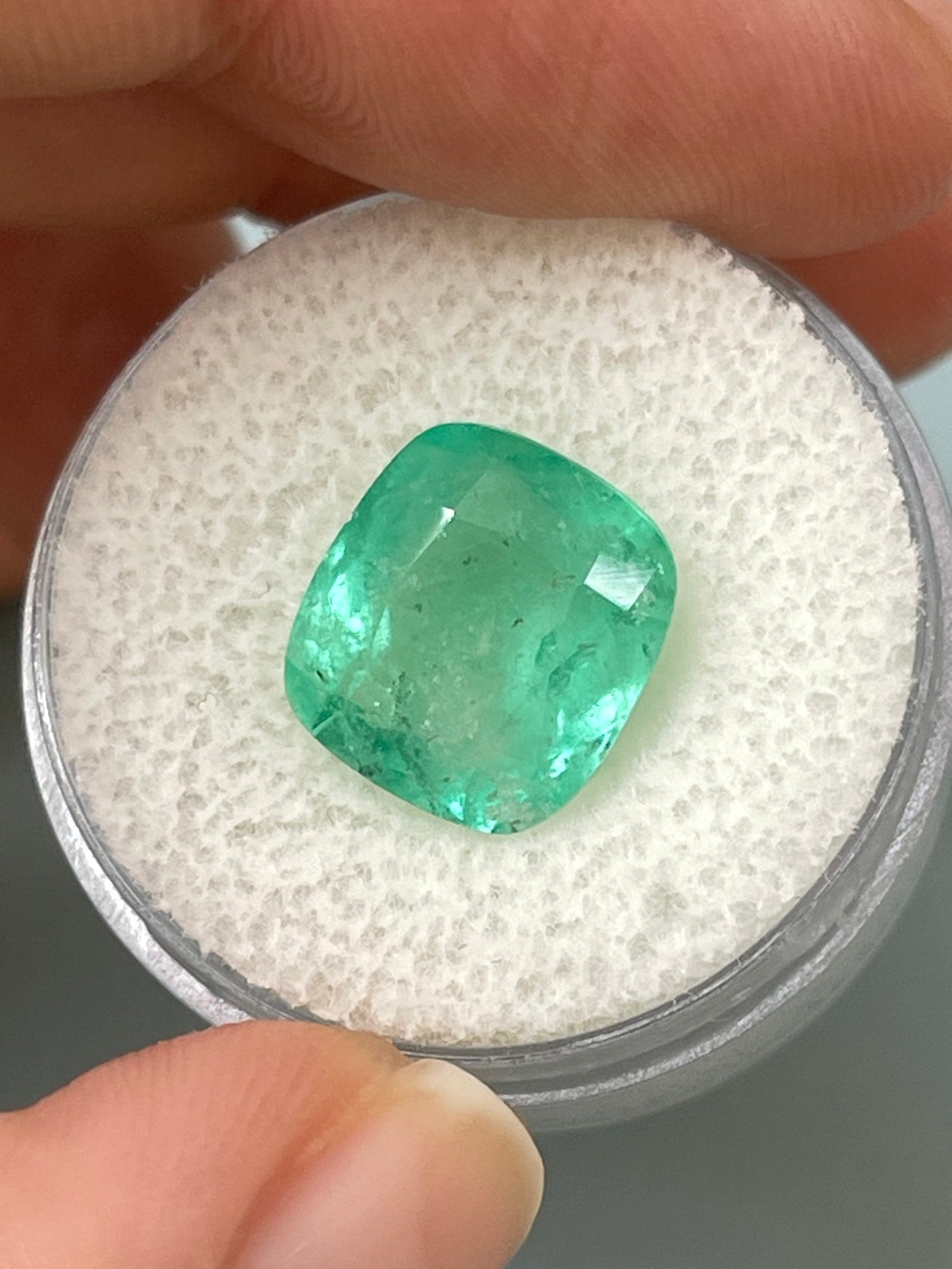 Loose 5.86 carat cushion cut Colombian emerald from JR Colombian Emeralds, showing its earthy pastel green hue and natural clarity.