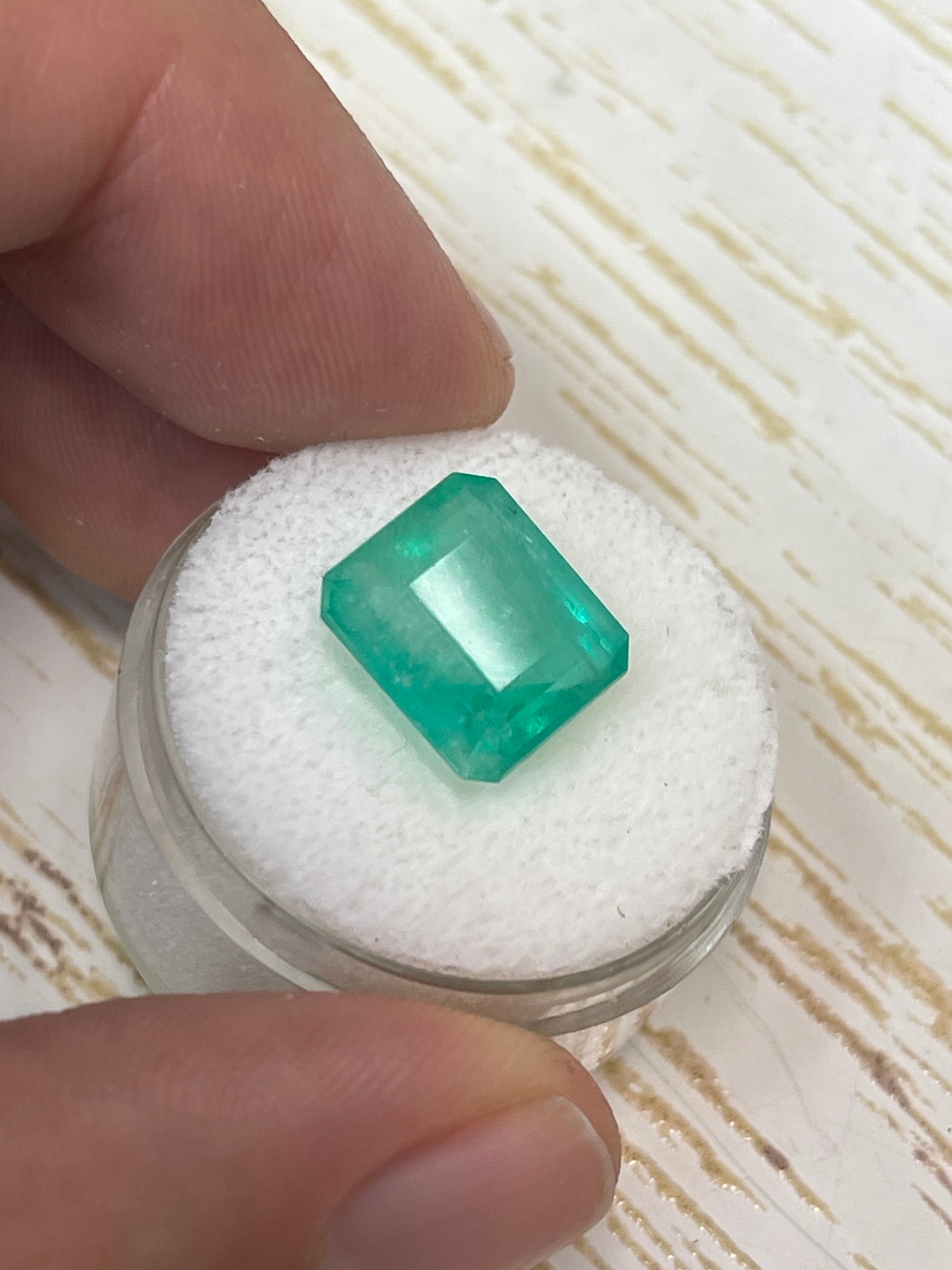 6.13 carat natural Colombian emerald loose gemstone with an emerald cut, featuring earthy pastel green color and clarity.