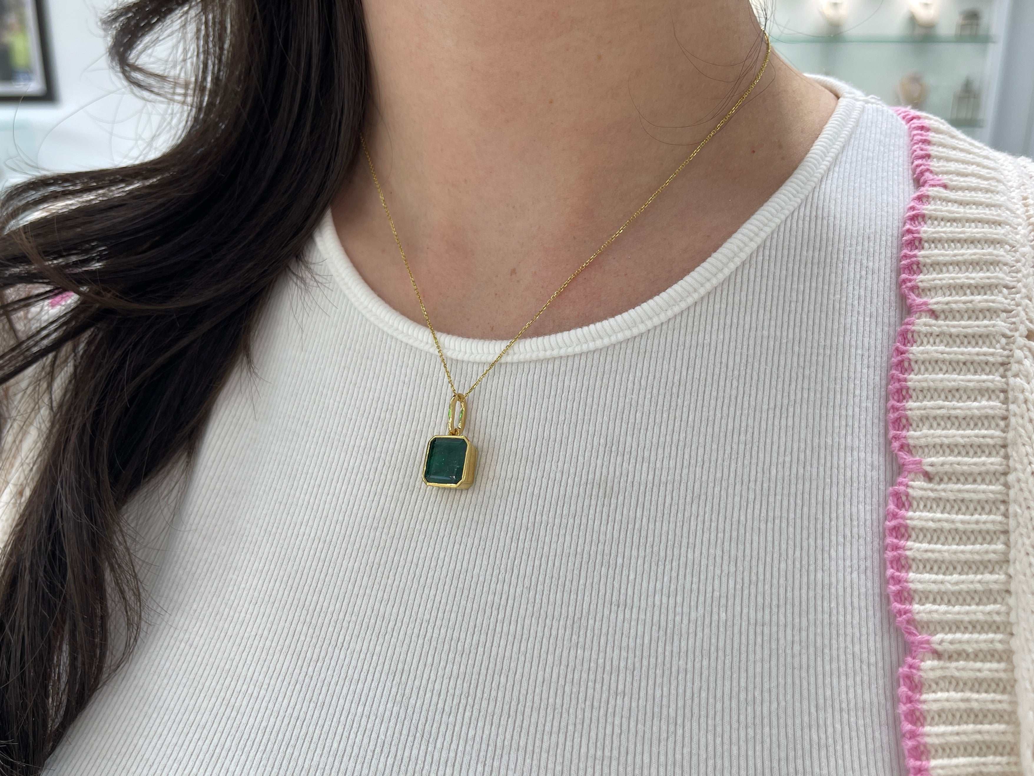 Dark green Zambian emerald necklace with a 7.79 carat bezel-set gemstone in 14K gold, featuring intricate jewelry design.