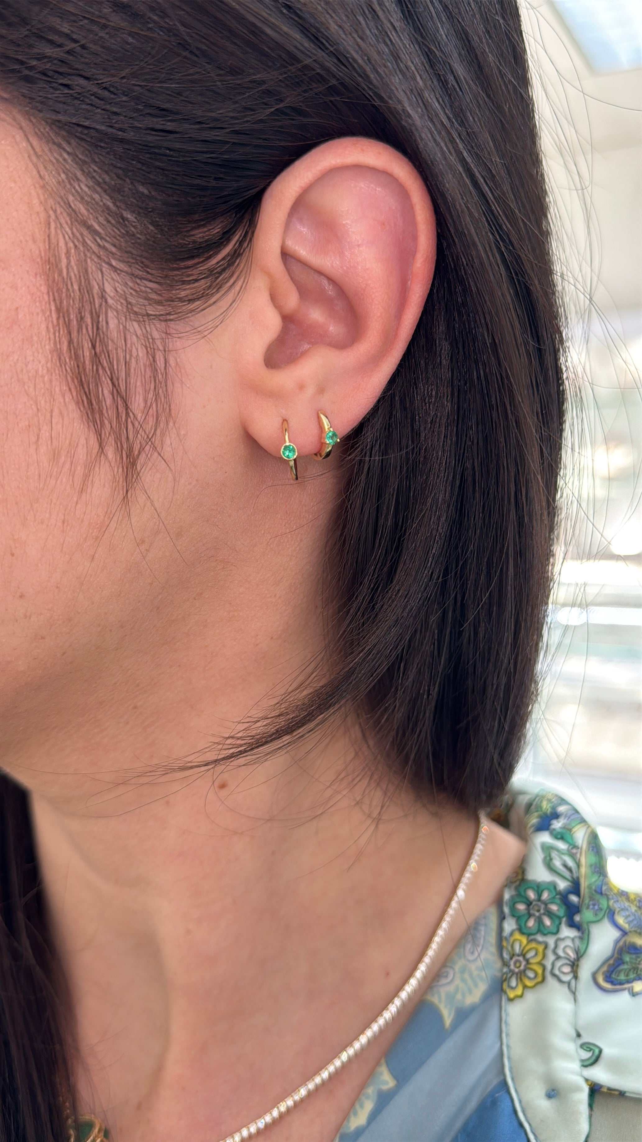 Emerald huggie earrings with three-prong settings in 14K gold from JR Colombian Emeralds, shown in a close-up image.