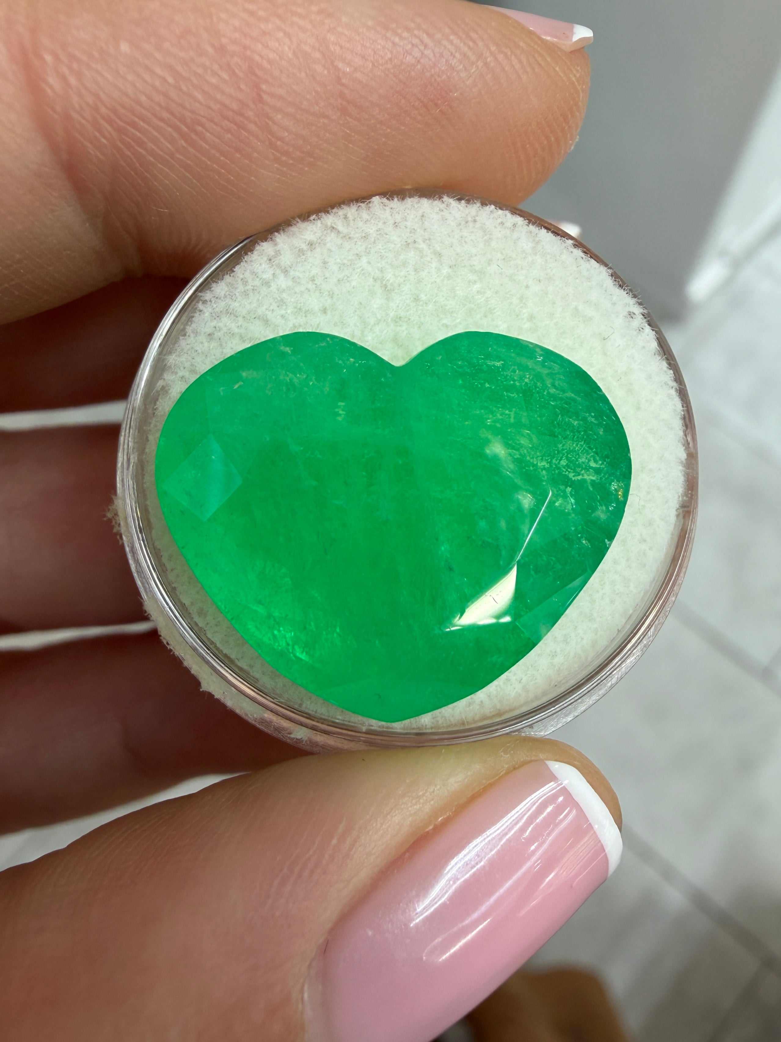 Large 23.97 carat bright green natural Colombian emerald loose gemstone in heart cut, showcasing vivid color and clarity.