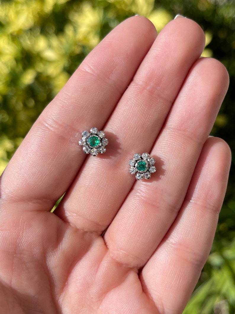 Colombian Emerald round cut diamond accent floral stud earrings in 14K gold featuring 0.44 tcw of gemstones.