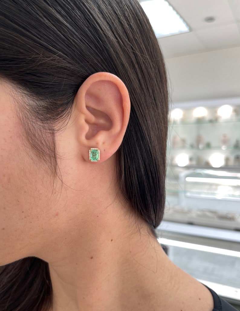 Colombian Emerald 14K gold halo stud earrings featuring 2.10tcw natural emerald-cut diamonds with a classic 9x7 design.