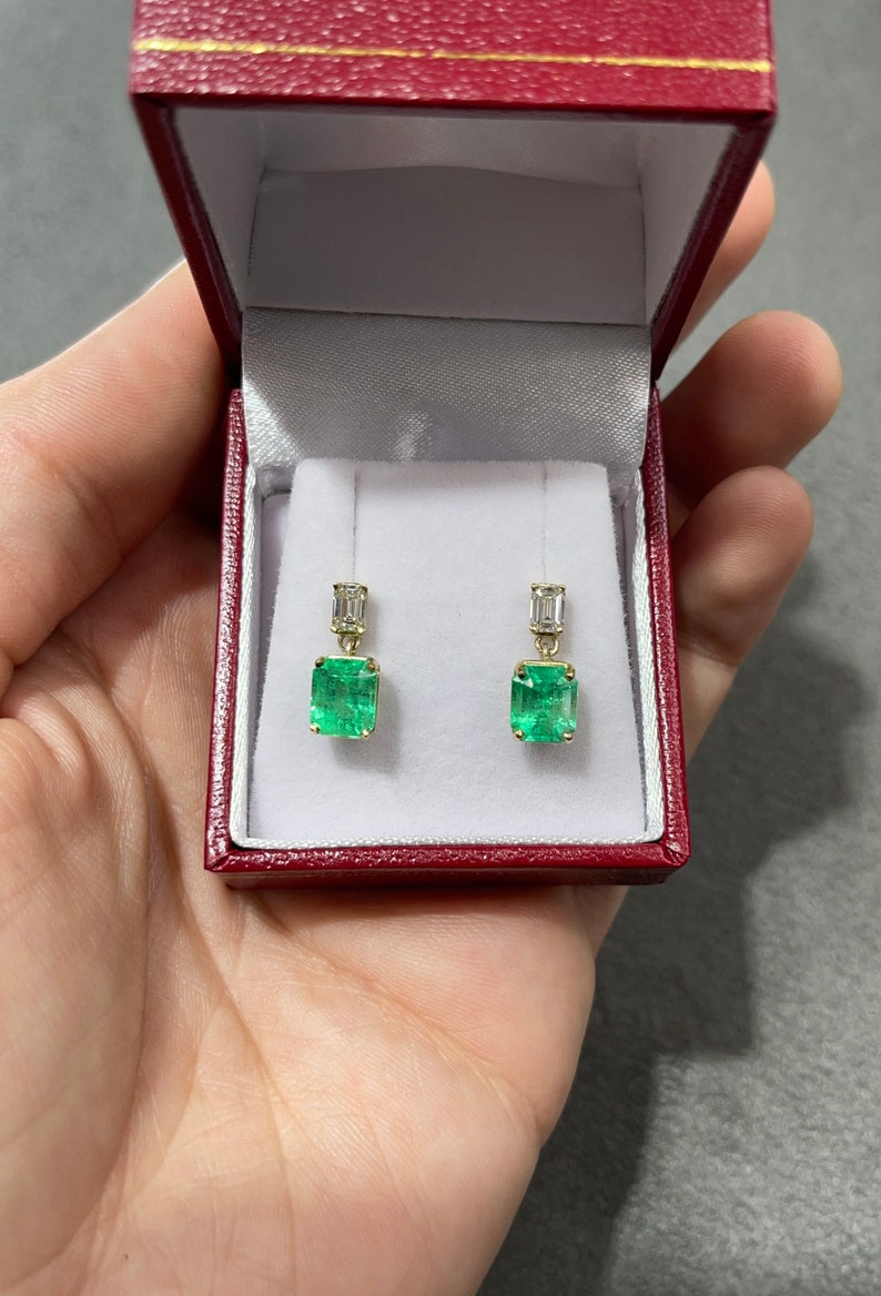 Elongated emerald and diamond dangle earrings in 18K gold featuring natural transparent Colombian emeralds and sparkling diamonds.