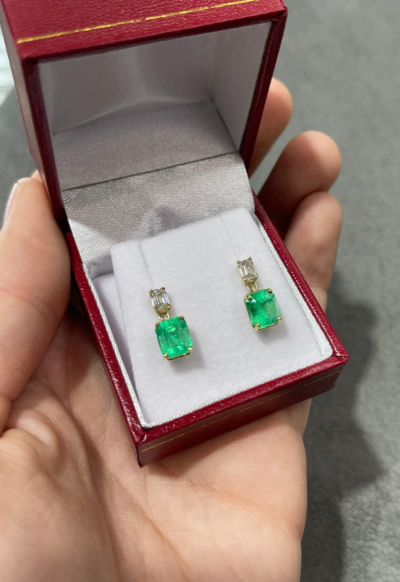 Elongated emerald and diamond dangle earrings in 18K gold featuring natural transparent gemstones and intricate detailing.