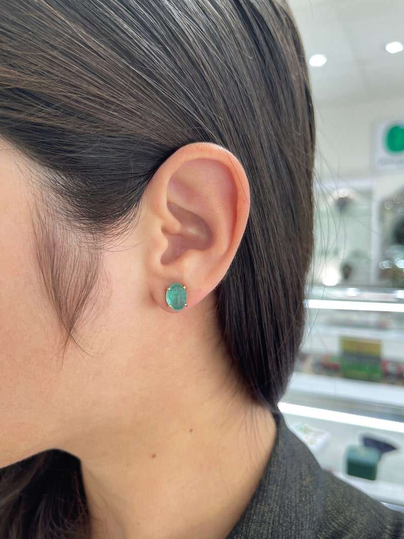 Colombian Emerald 14K stud earrings featuring 4.34tcw oval cut deep bluish green natural emeralds on a white background.
