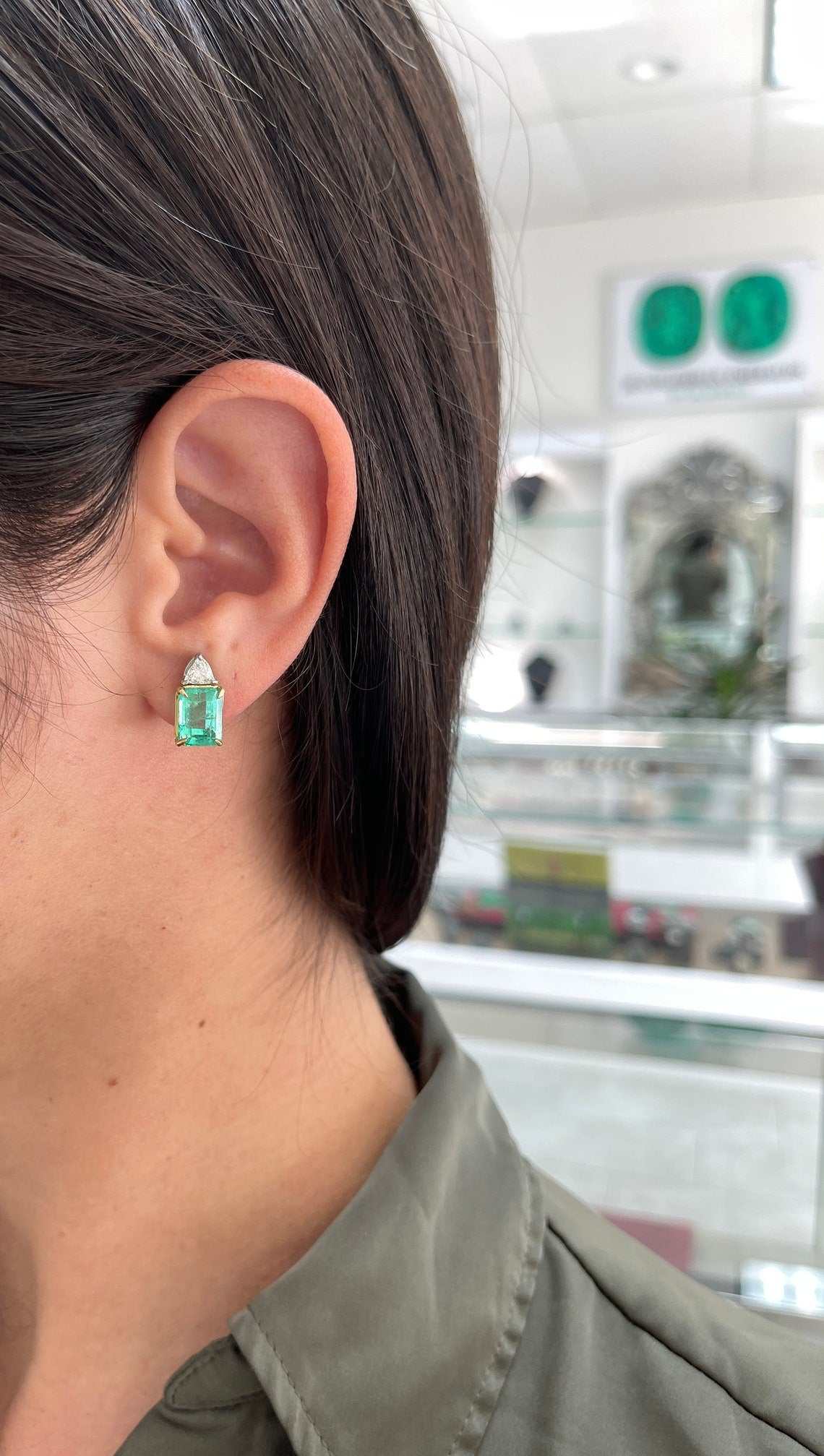 Colombian Emerald brand earrings featuring 6.73tcw platinum 18K two-stone stud earrings with emerald cut and diamond trillion accents.