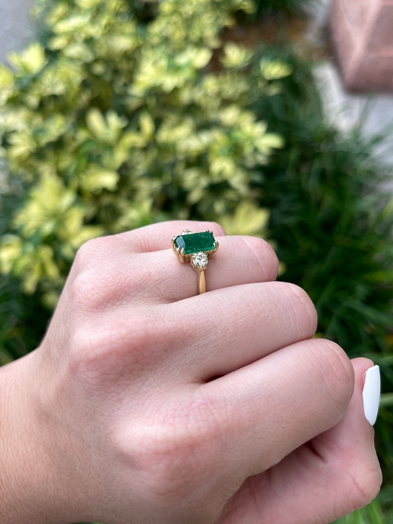 Colombian Emerald 18K gold three-stone engagement ring featuring a deep dark alpine green emerald cut and round diamonds.