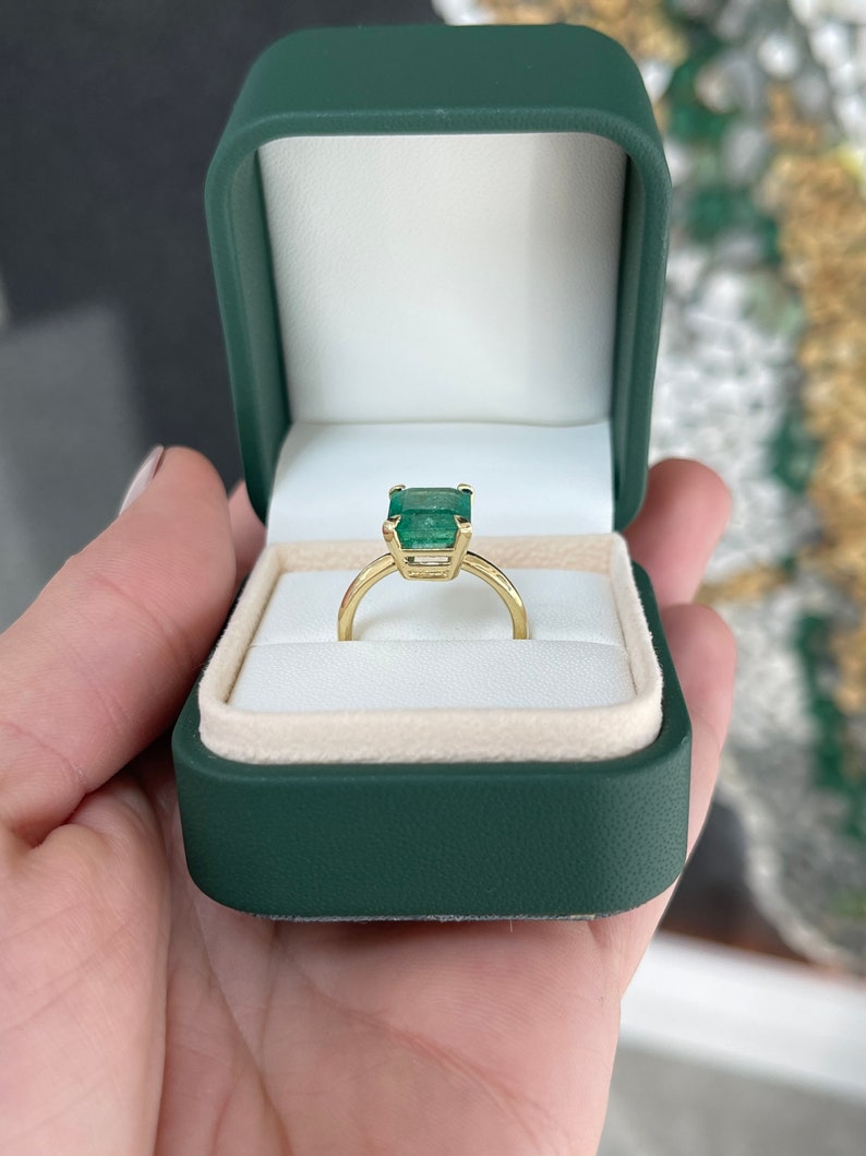 18K yellow gold emerald cut solitaire engagement ring with four prongs and half-bezel setting, featuring a 4.10 carat Colombian emerald.