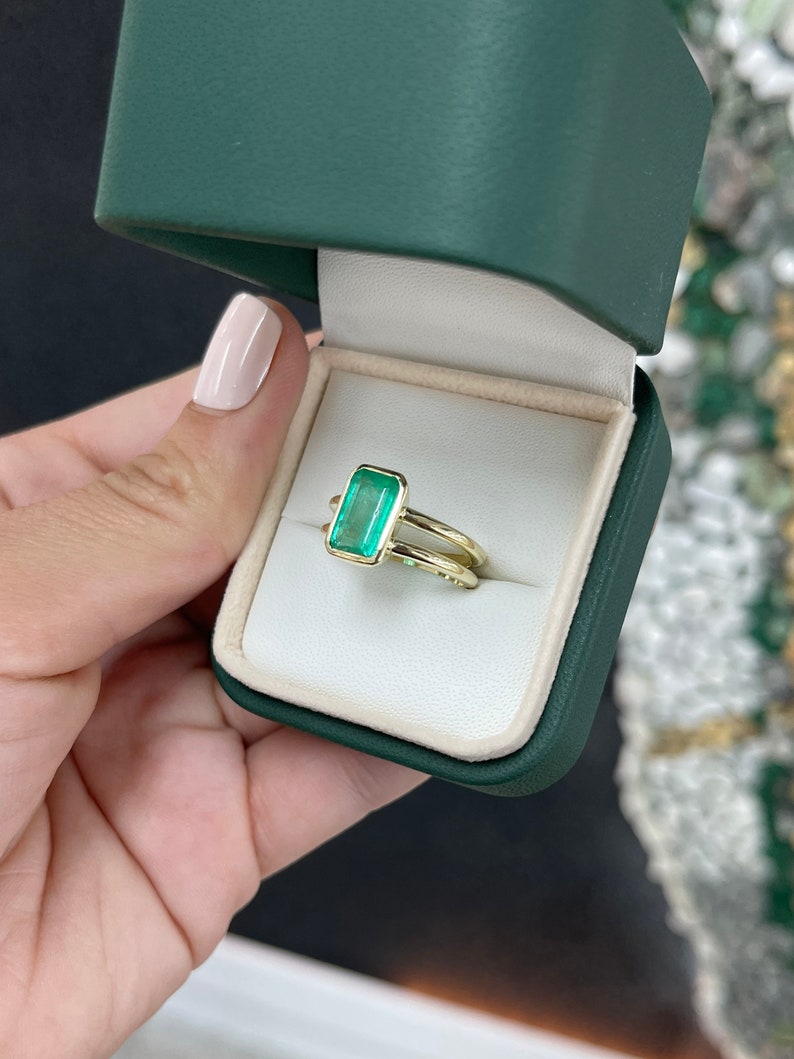 Colombian Emerald ladies ring featuring a 2.05ct vivid green emerald cut solitaire gemstone in 14K gold with split shank design.