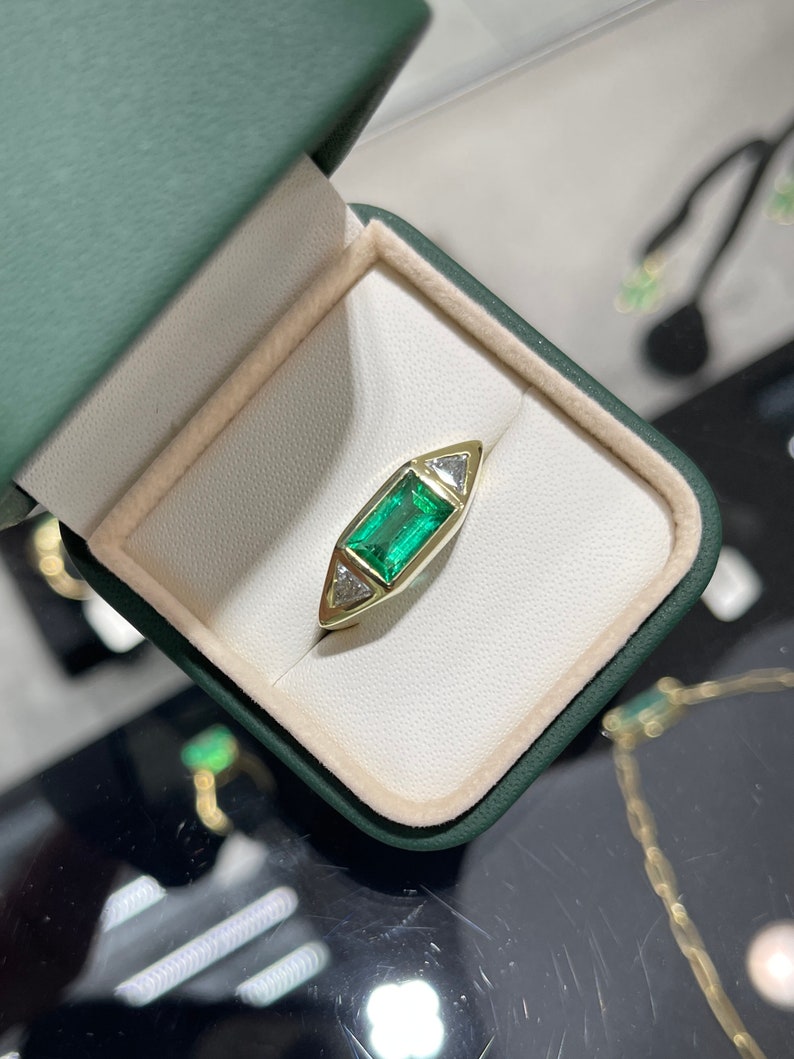 Ladies emerald ring featuring 2.35tcw three-stone design with baguette, trillion cut diamonds, 18K AAA quality, Colombian Emerald brand.