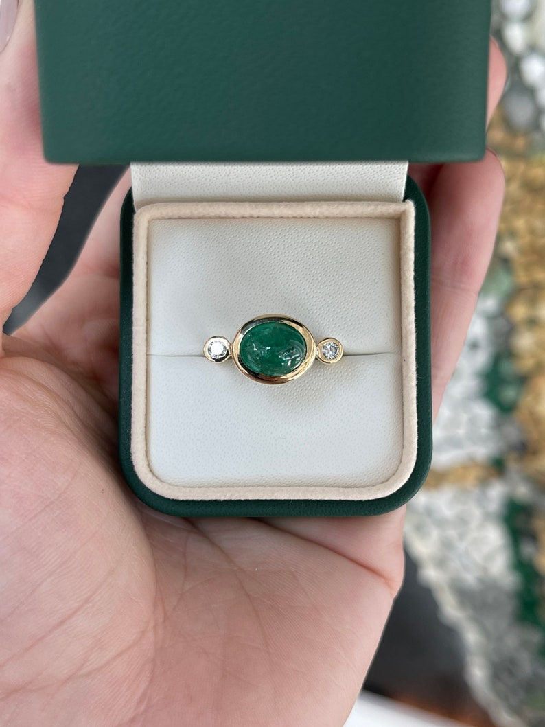Ladies Colombian Emerald ring featuring a 4.50tcw oval dark green emerald cabochon with diamond accents in 14K gold.