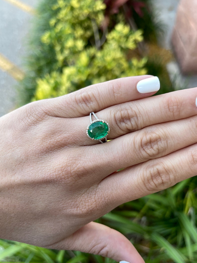 14K Colombian Emerald and diamond halo engagement ring with oval emerald center and split shank design, featuring intricate detailing.