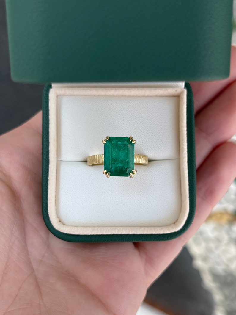 18K matte hammered gold emerald cut solitaire ring with dark green rustic Colombian emerald and double claw prongs.