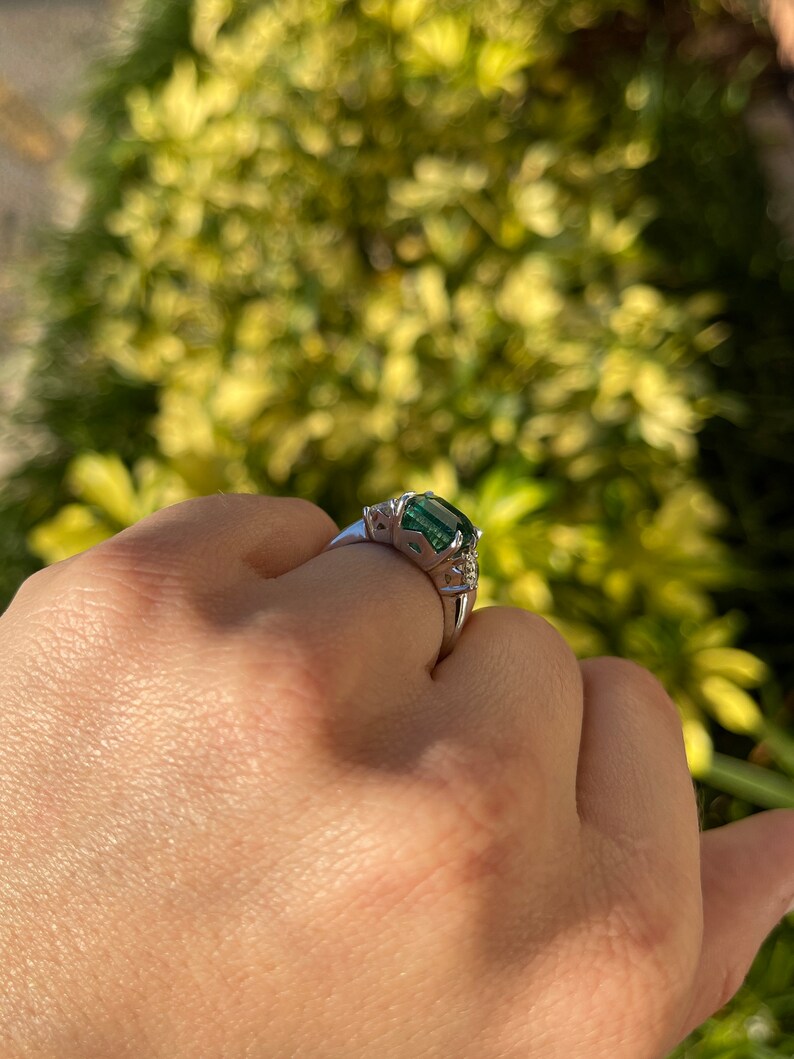 14K gold 3-stone engagement ring featuring intense dark green Asscher cut emerald and round diamonds from Colombian Emerald.