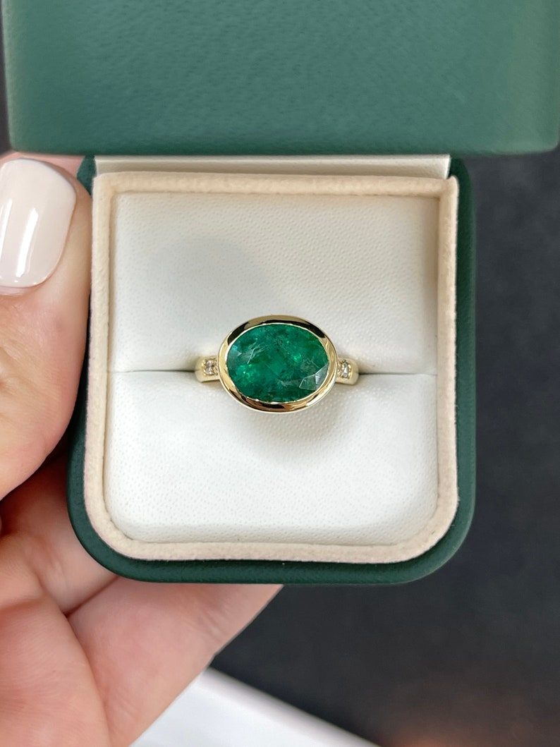 18K gold ring with a 5.66tcw dark green oval bezel emerald and diamond accents, Colombian Emerald brand jewelry.