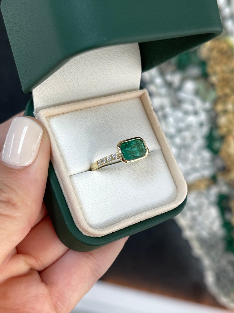 14K gold ring featuring a natural emerald cut emerald with bezel setting and diamond shank, Colombian Emerald brand.