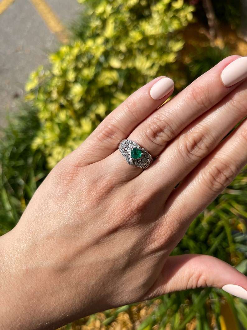 14K Colombian Emerald and diamond cluster statement ring featuring a 0.90tcw trilliant cut emerald and sparkling accents.