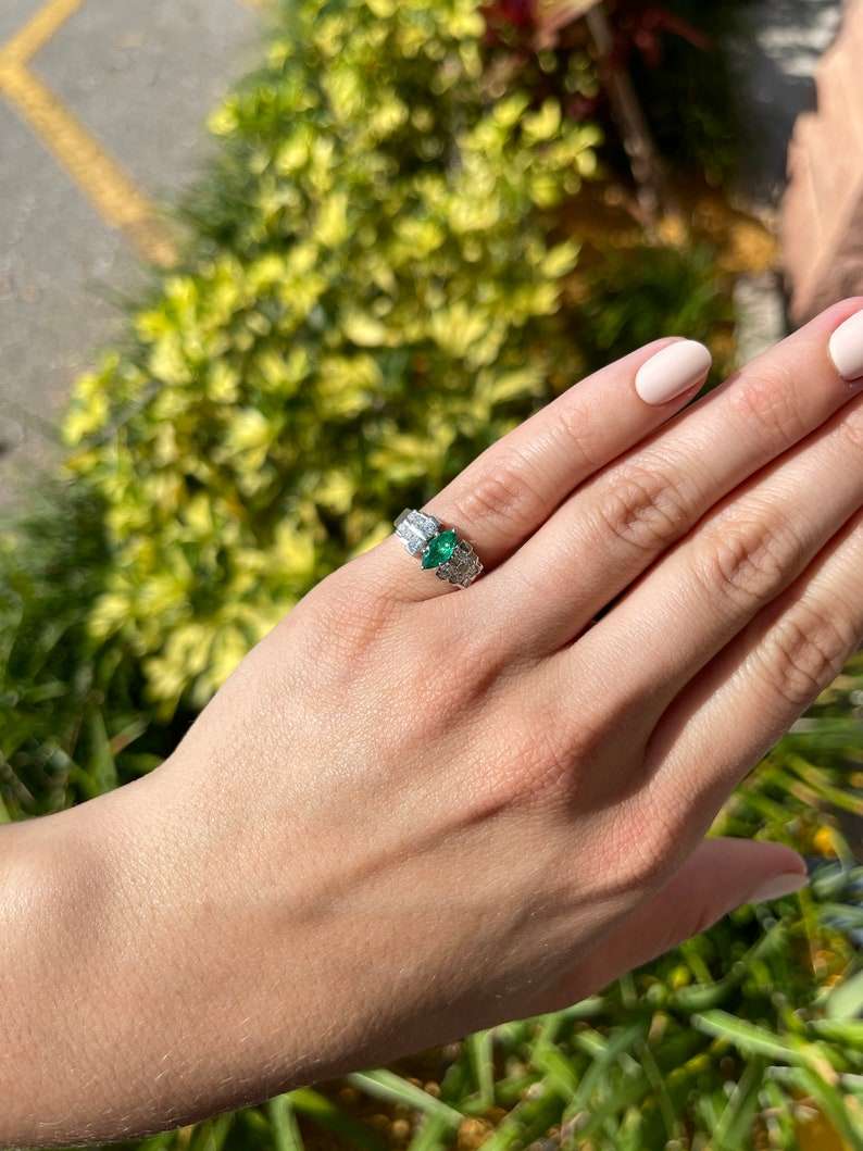 Colombian Emerald marquise diamond cocktail ring in platinum with semi-transparent band and intricate gemstone setting.