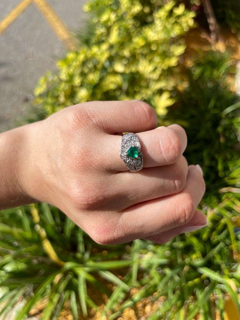 14K Colombian Emerald and diamond cluster statement ring featuring a 0.90tcw trilliant cut emerald and sparkling accents.