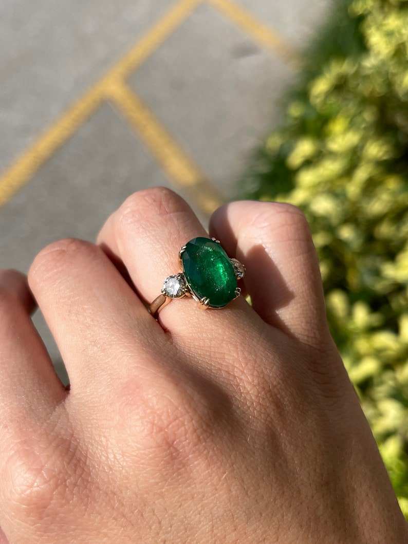 Dark green oval emerald and round diamonds on 14K Colombian Emerald engagement ring with double prong setting.