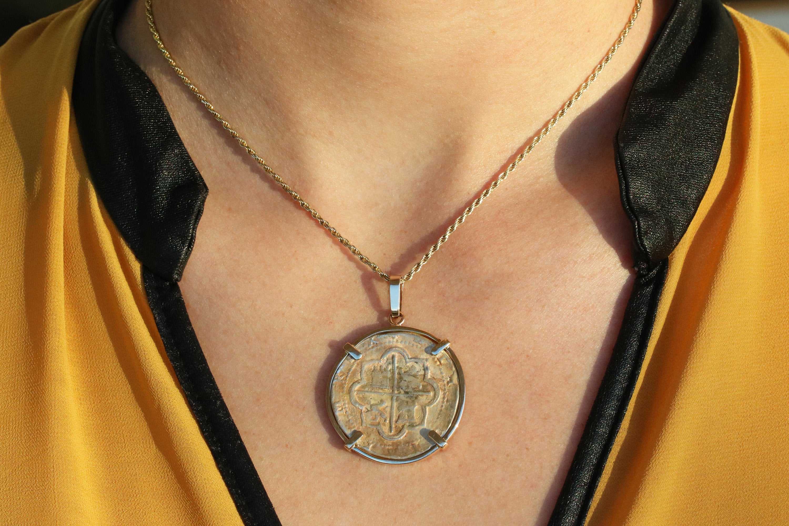 silver Atocha coin replica pendant in 14K gold bezel worn on neck with yellow and black shirt