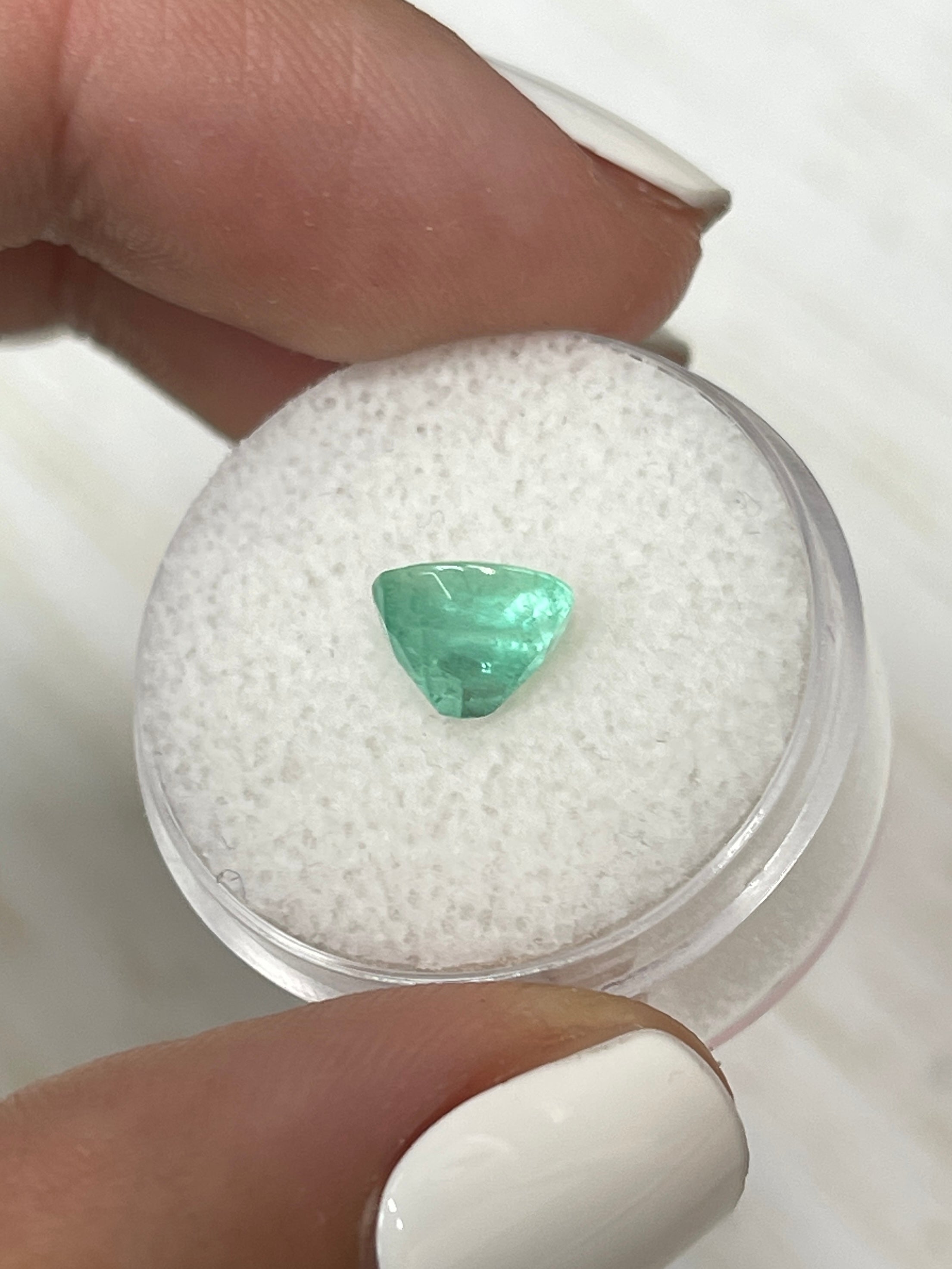 Light spring green oval cut Colombian emerald, 1.55 carats, showcasing its natural beauty and clarity against a neutral background.