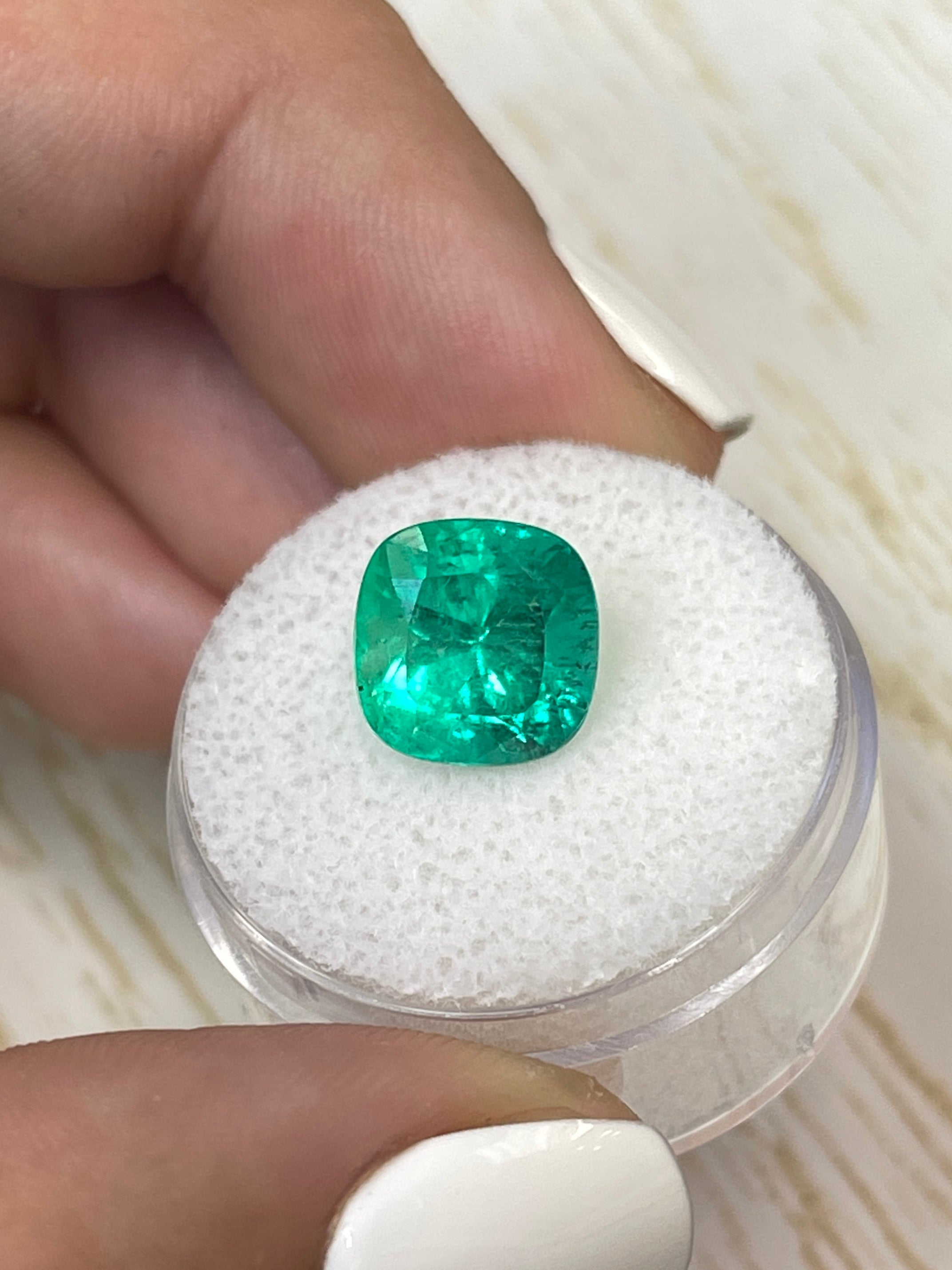 Bright green 4.72 carat Colombian emerald in cushion cut, showcasing natural facets and rich color against a neutral background.