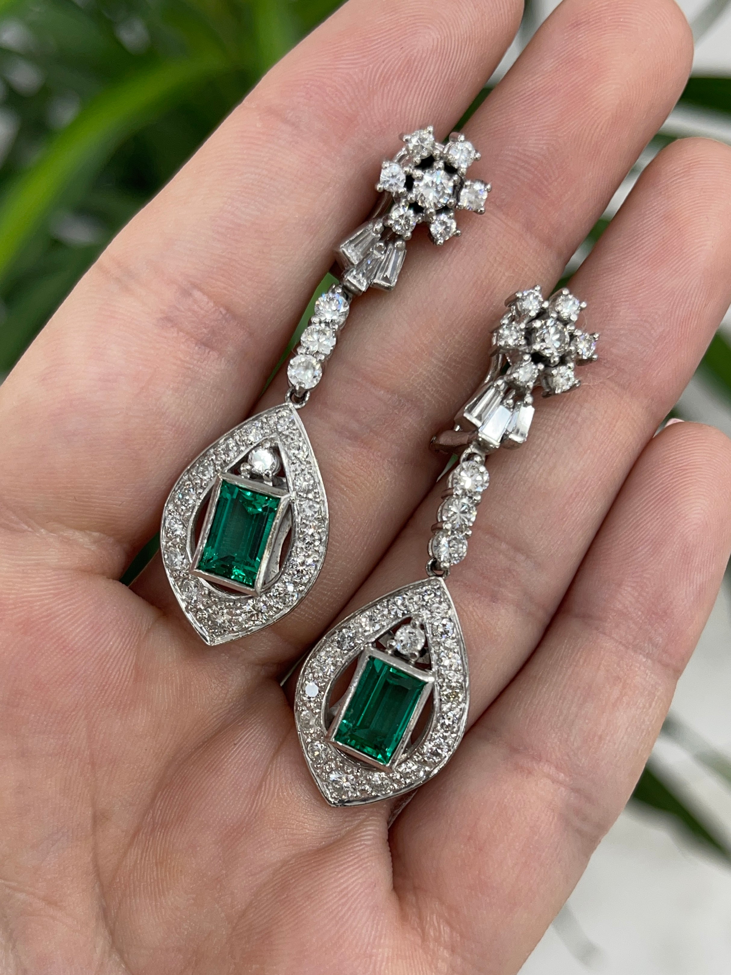 Art Deco Colombian emerald and diamond dangle earrings in 18K gold featuring intricate design and vibrant green gemstones.