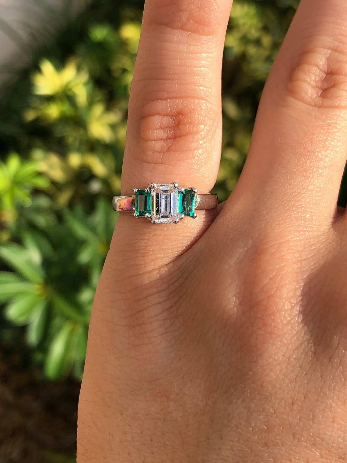 Natural-looking 14K gold engagement ring with three-stone diamonds and emeralds, showcasing elegant craftsmanship and sparkling gemstones.