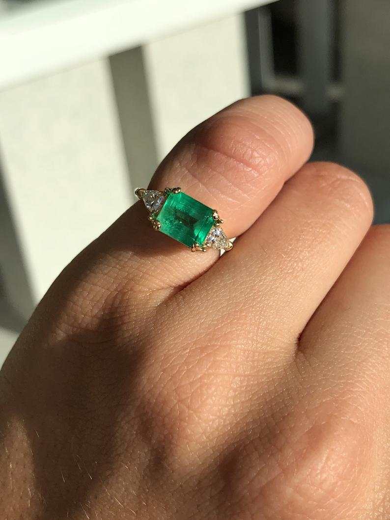 Three-stone engagement ring with emerald cut Colombian emerald and trillion diamonds in 18K gold, by JR Colombian Emeralds.