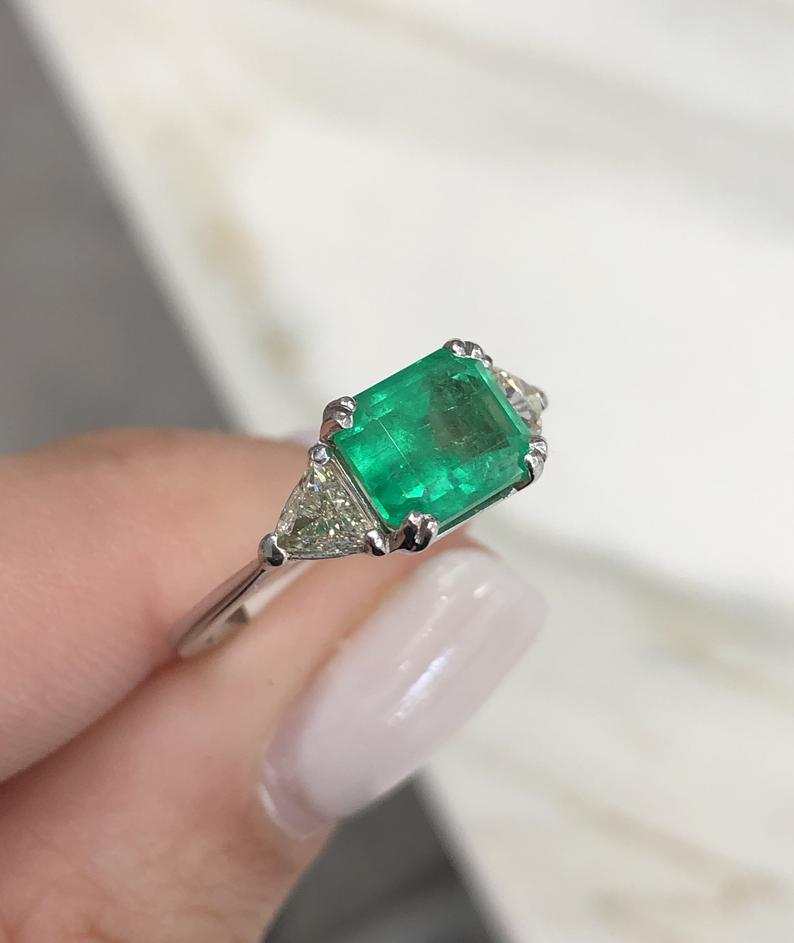 Three stone emerald cut Colombian and trillion diamond engagement ring by JR Colombian Emeralds, 18K gold, east-to-west design.