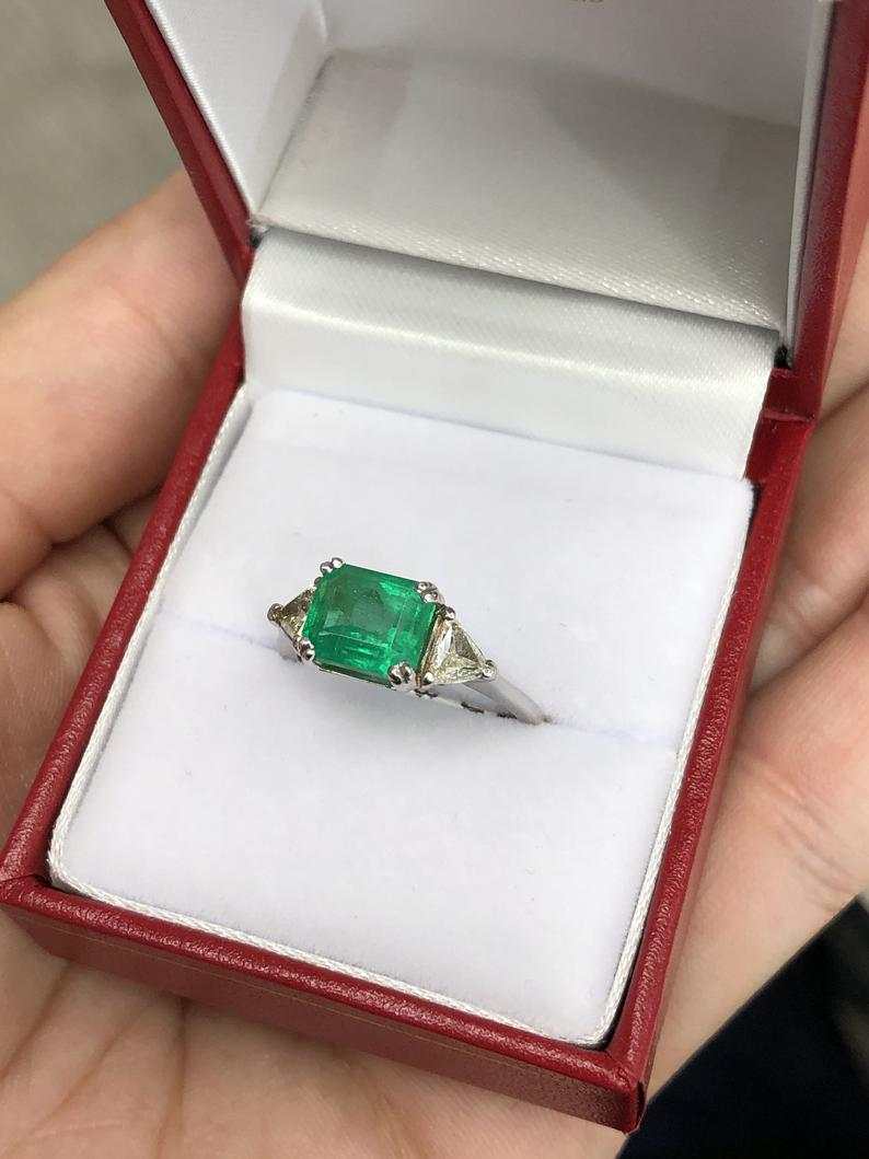 Three-stone emerald cut engagement ring with Colombian emeralds and trillion diamonds in 18K gold by JR Colombian Emeralds.
