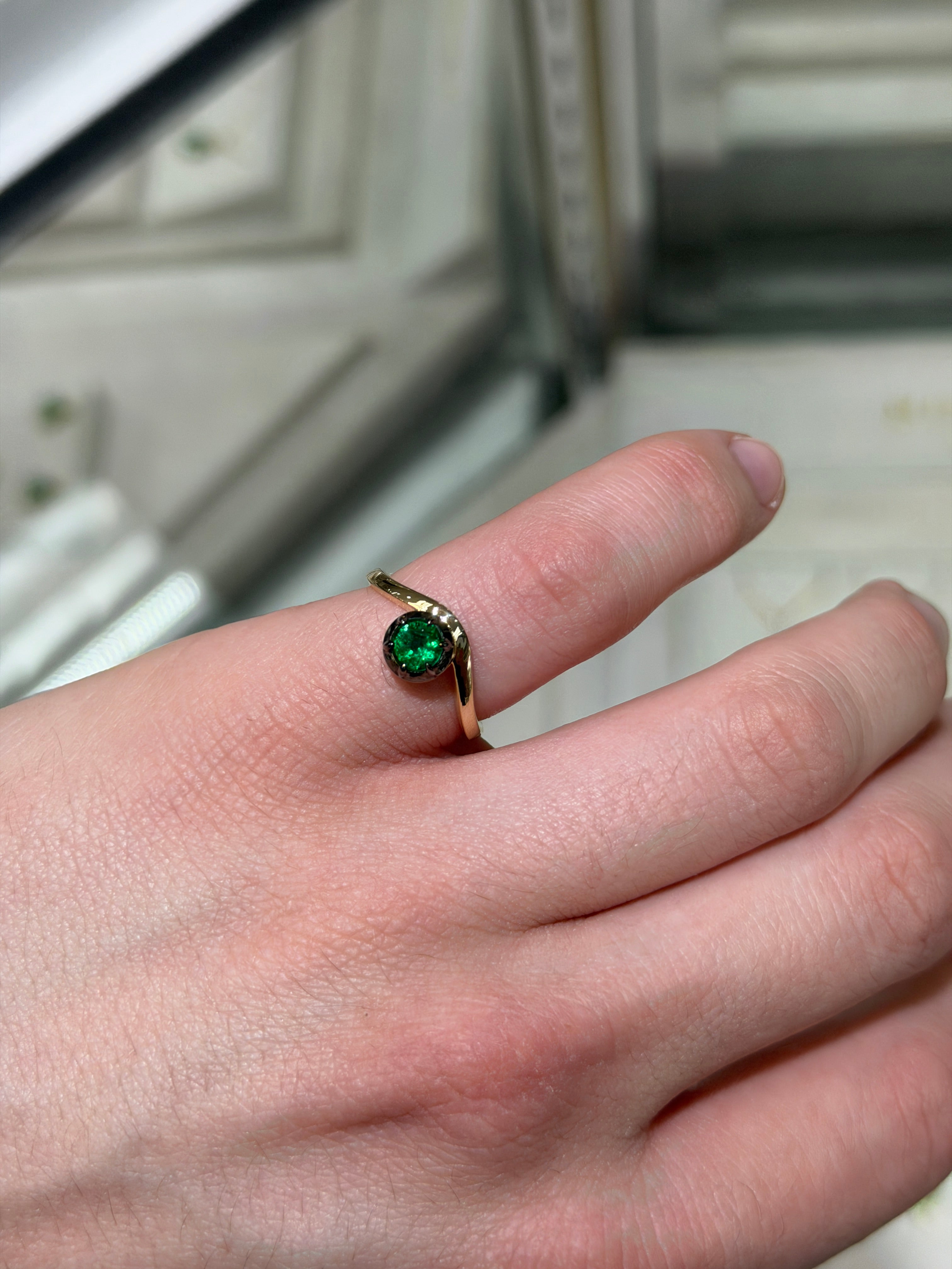 Ladies emerald ring by JR Colombian Emeralds featuring a 0.64ct round cut emerald in a 14K gold multi-prong setting with black rhodium finish.