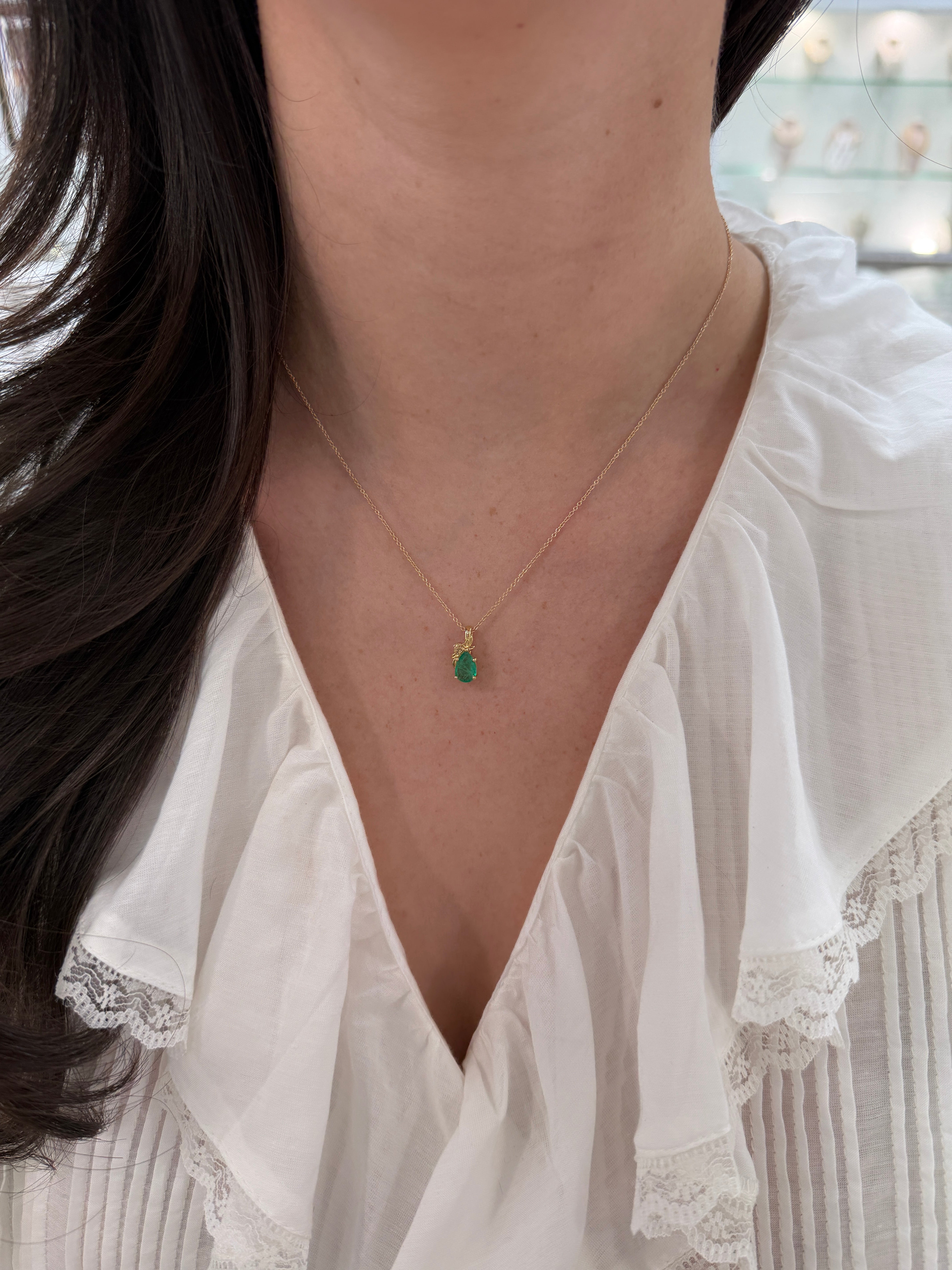 14K gold pendant necklace featuring a 1.0ct natural medium green pear-cut emerald in a floral solitaire setting.